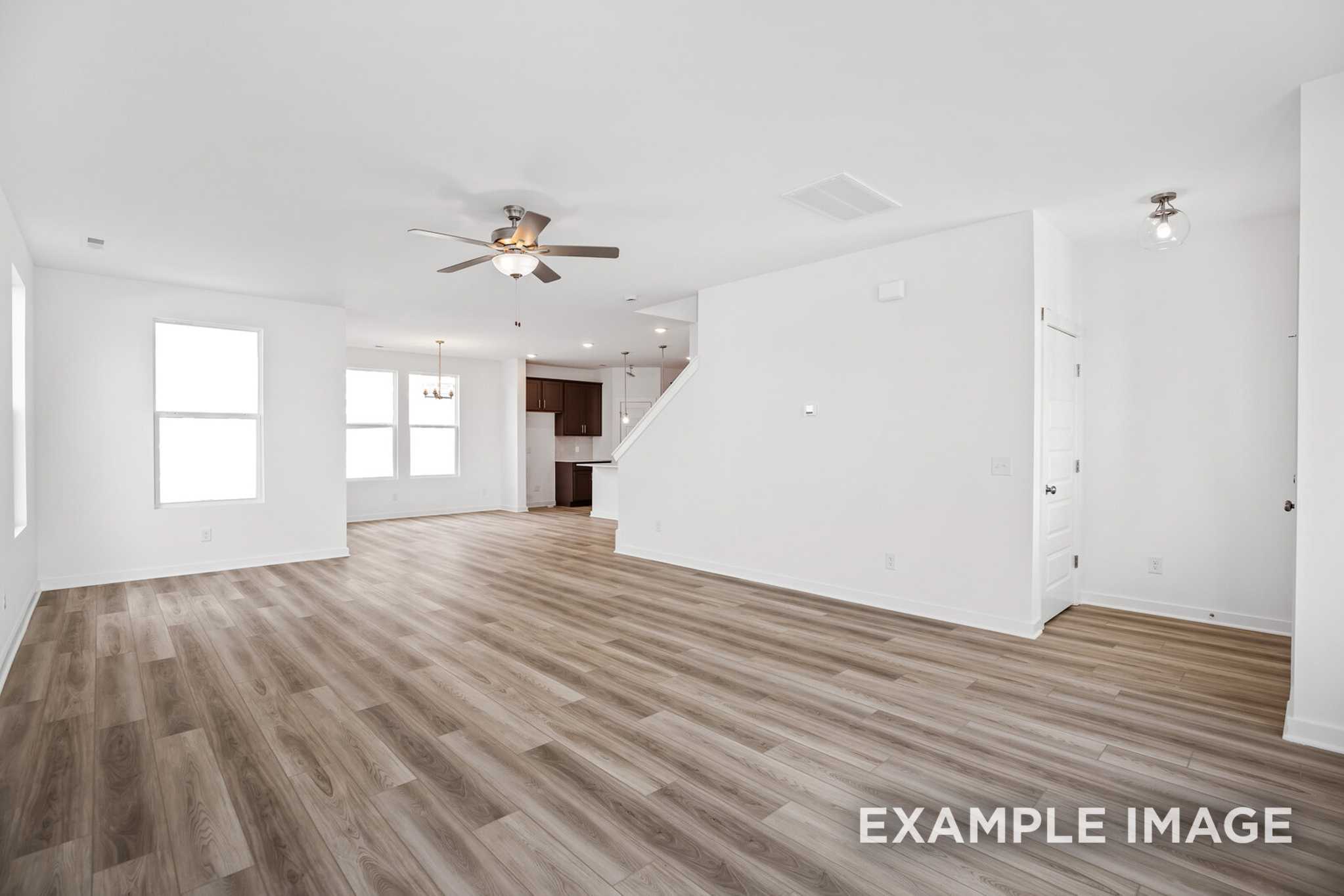 Spacious open-concept living area in The Murray B home with hardwood floors, large windows, ceiling fan, and staircase