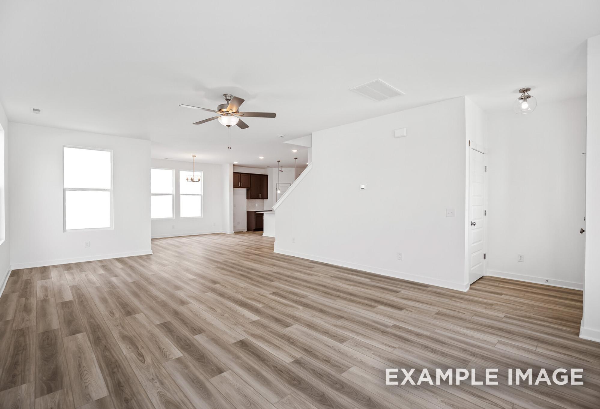 Spacious open-concept living area in The Murray B home with hardwood floors, large windows, ceiling fan, and staircase