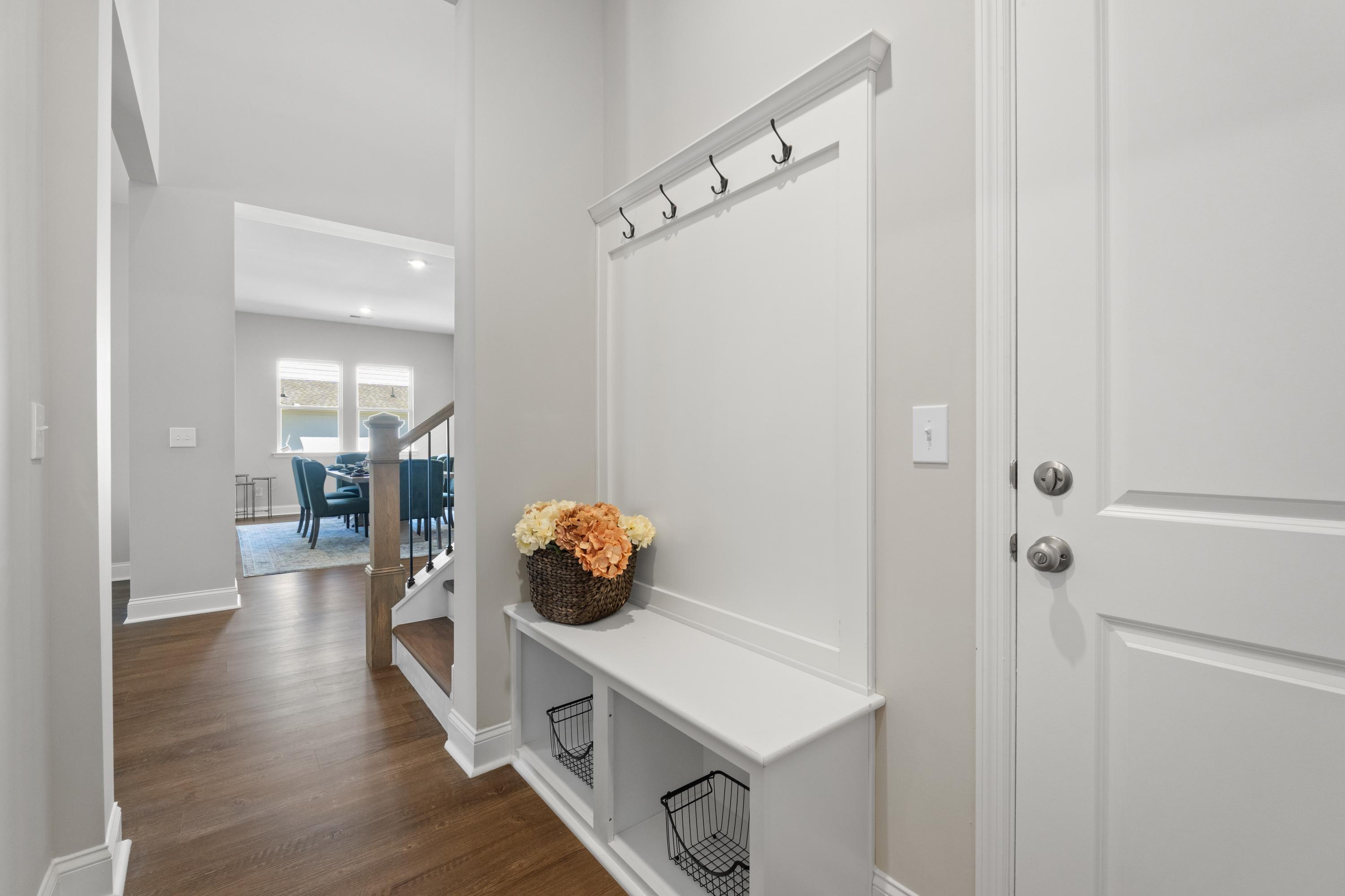 The Haven entryway featuring white built-in bench, coat hooks, orange floral vase, and open dining view