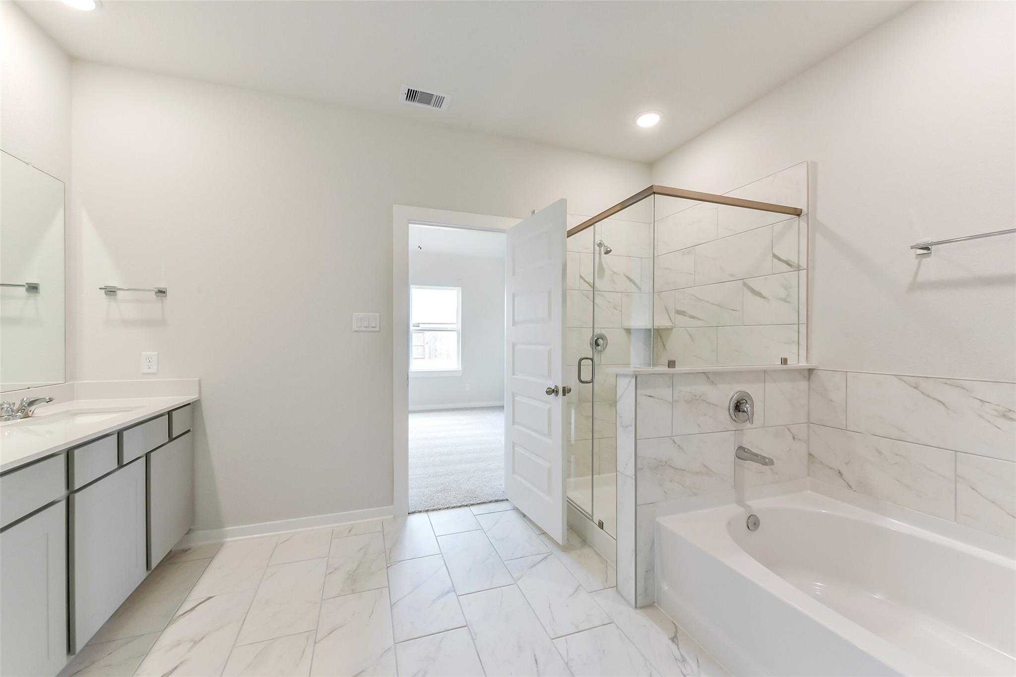 Modern master bathroom with glass shower, soaking tub, double vanity, and tiled floors in Davidson Homes The Laguna C, Rosharon, Texas