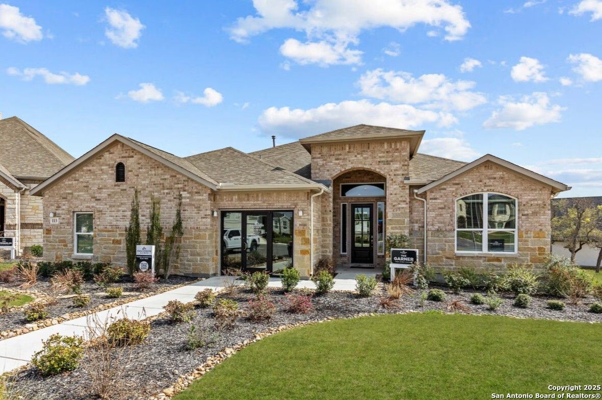 Tan brick one-story home with arched entry, double garage doors, and landscaped yard in Ladera, San Antonio – Davidson Homes The Garner B