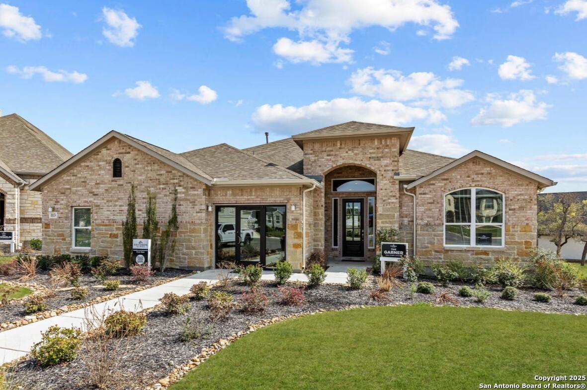 Tan brick one-story home with arched entry, double garage doors, and landscaped yard in Ladera, San Antonio – Davidson Homes The Garner B