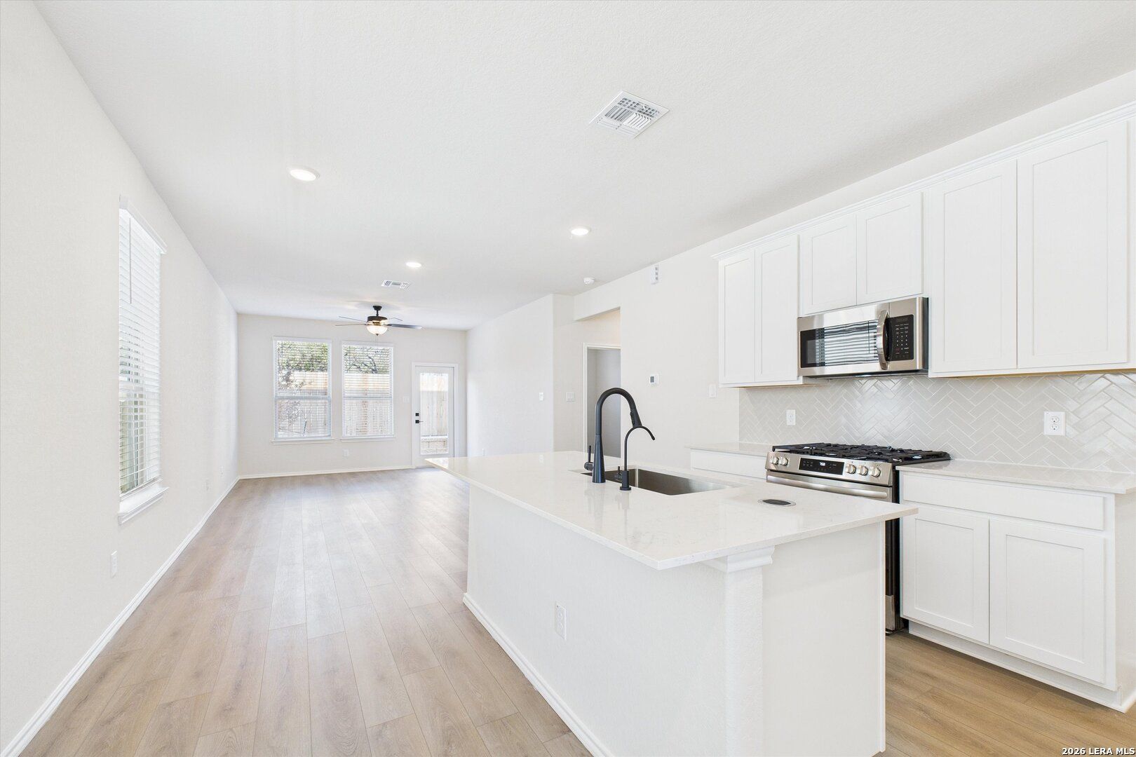 Modern white kitchen with stainless appliances, quartz island, and open living area in The Gillian B 4-bedroom home, San Antonio, Texas