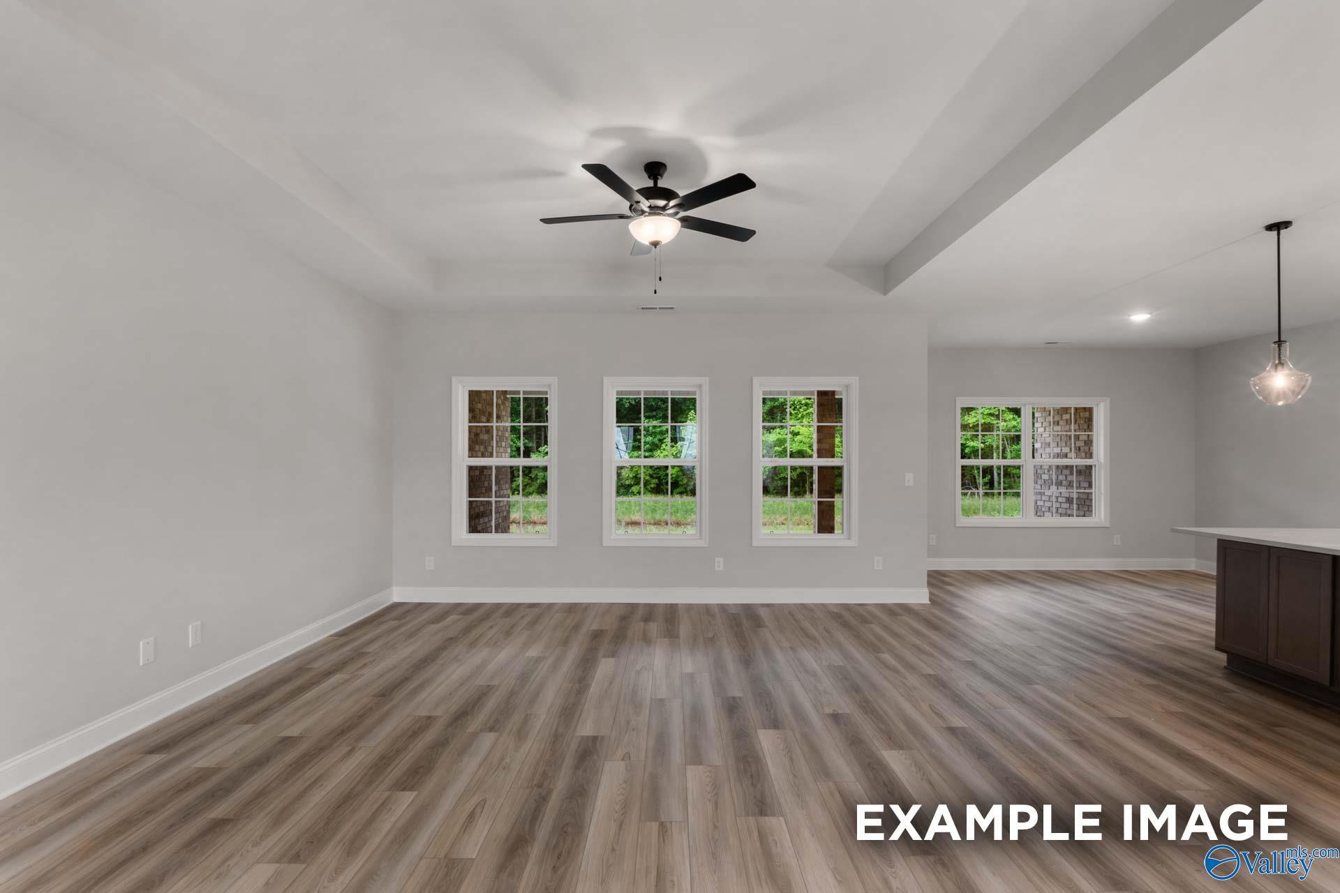 Spacious living room with large windows overlooking greenery, ceiling fan, light wood floors in Davidson Homes The Finleigh, Meridianville, Alabama