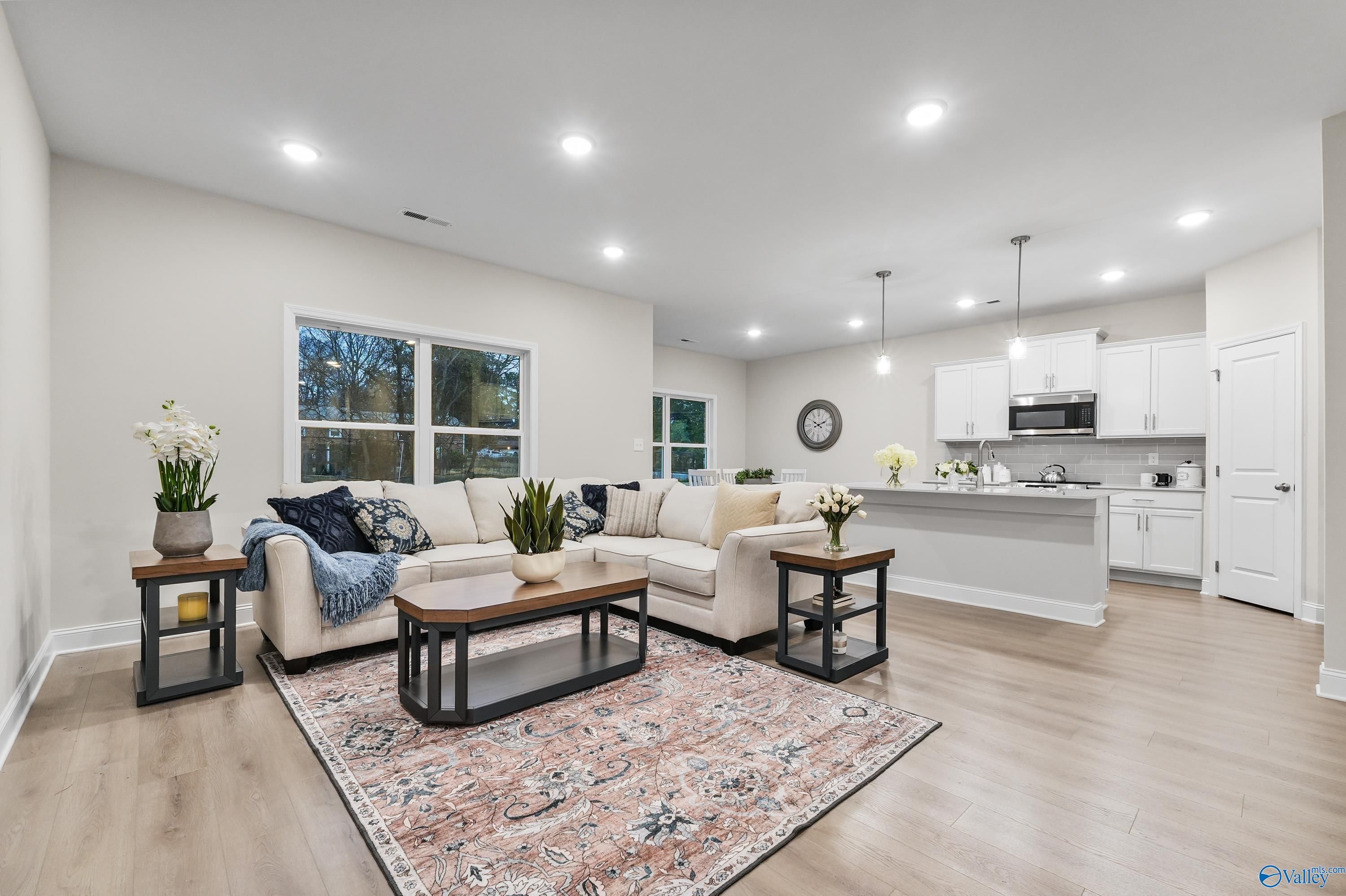 Open-concept living room with beige L-shaped sofa, plants, rug, and white kitchen island in Davidson Homes The Asheville C, Huntsville AL