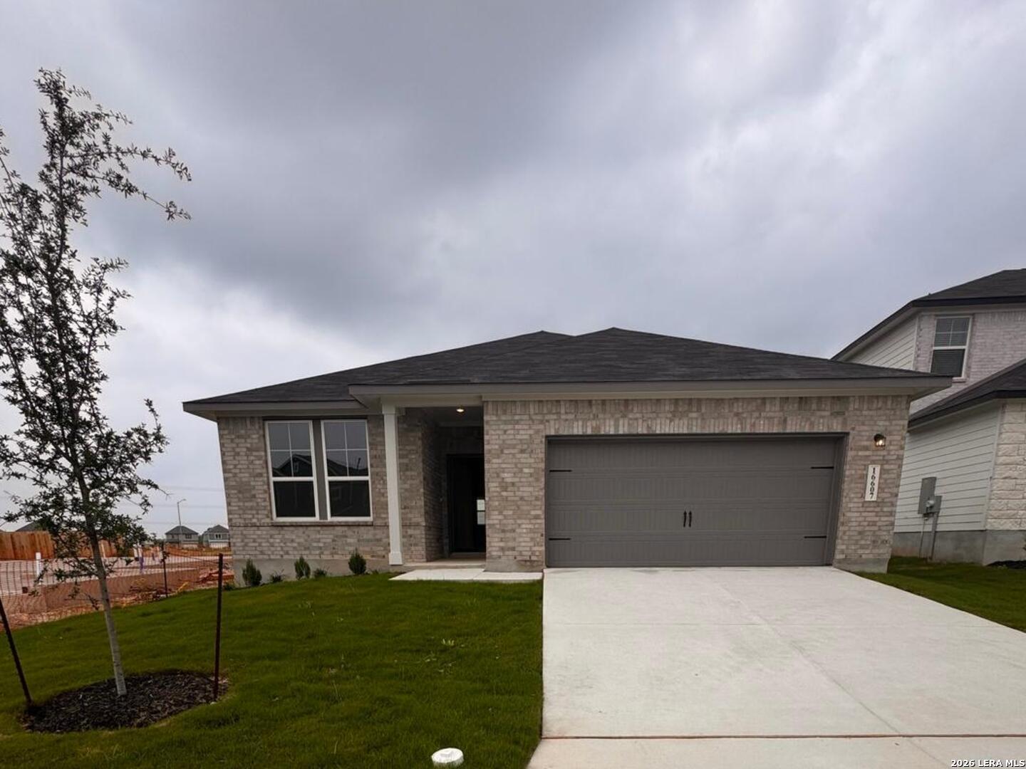 Modern brick single-story home with 2-car gray garage, covered entry, and sodded lawn in Hickory Ridge, Elmendorf, Texas - Davidson Homes Glenwood E