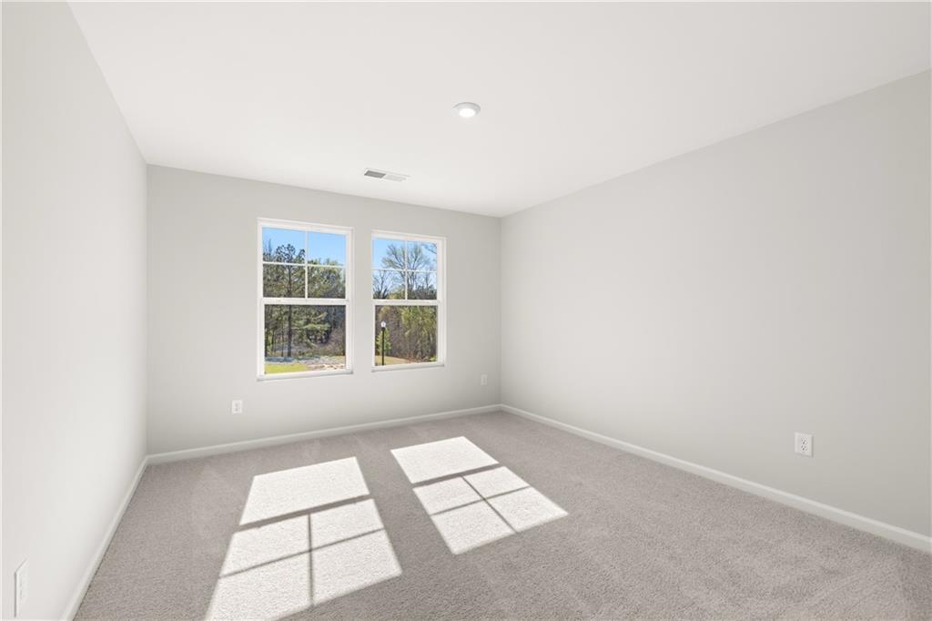Bright bedroom with light gray walls, double windows, and sunlit carpet in Davidson Homes The Cary A, Winder, Georgia