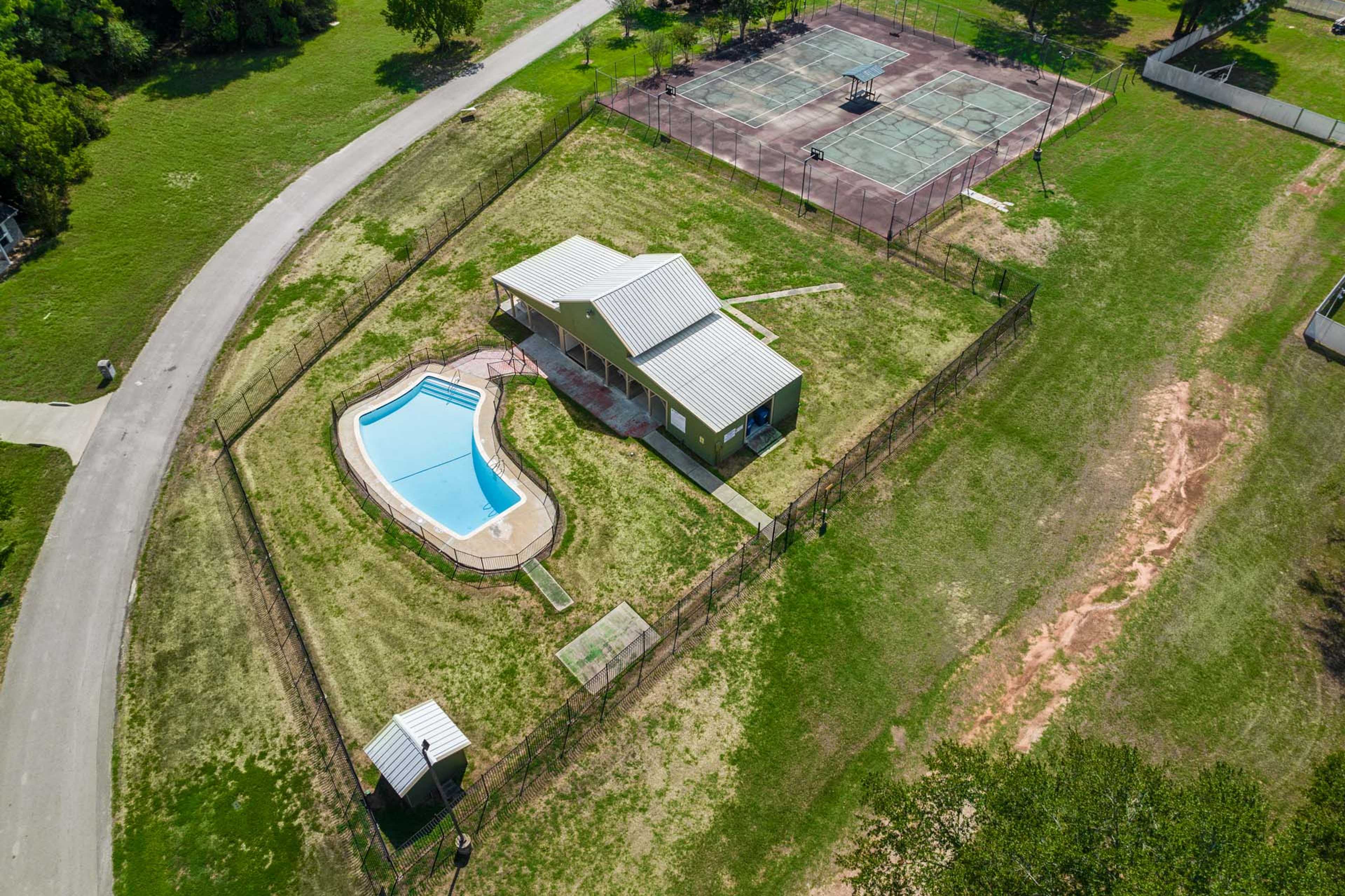 Aerial view of kidney-shaped pool, pavilion, and tennis courts surrounded by green lawns at Windmill Estates in Magnolia, Texas