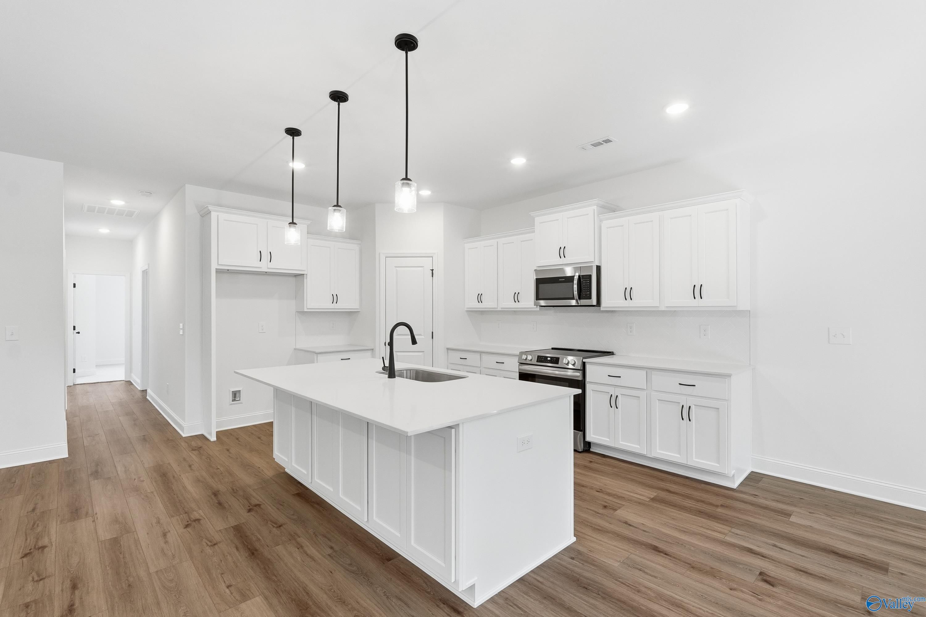 Modern white kitchen with island sink, stainless appliances, and pendant lights in Davidson Homes The Rockford D, Hazel Green, AL