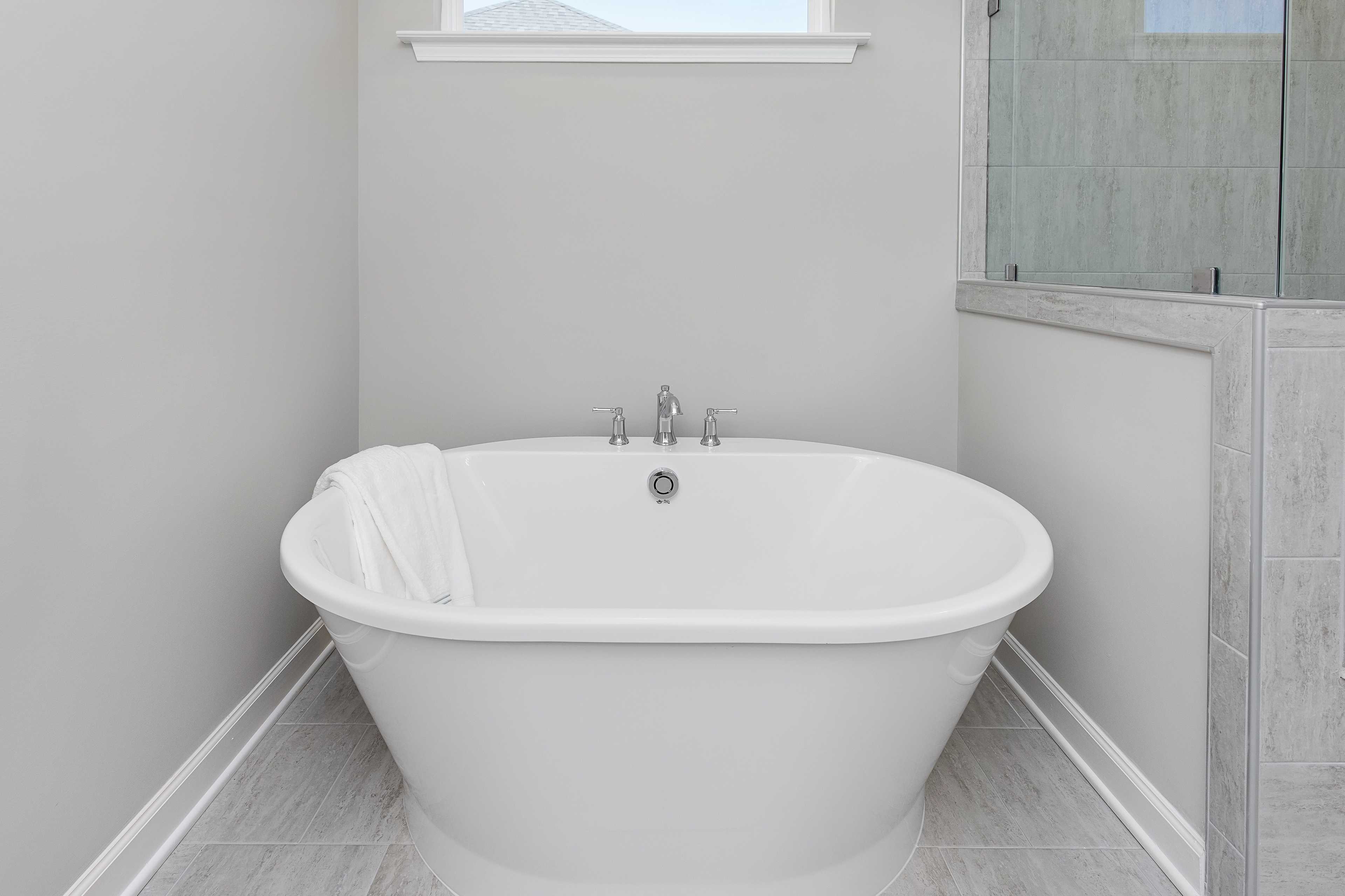 Elegant freestanding oval soaking tub with white towel in modern bathroom at Woodland Crossing, Zebulon NC by Davidson Homes
