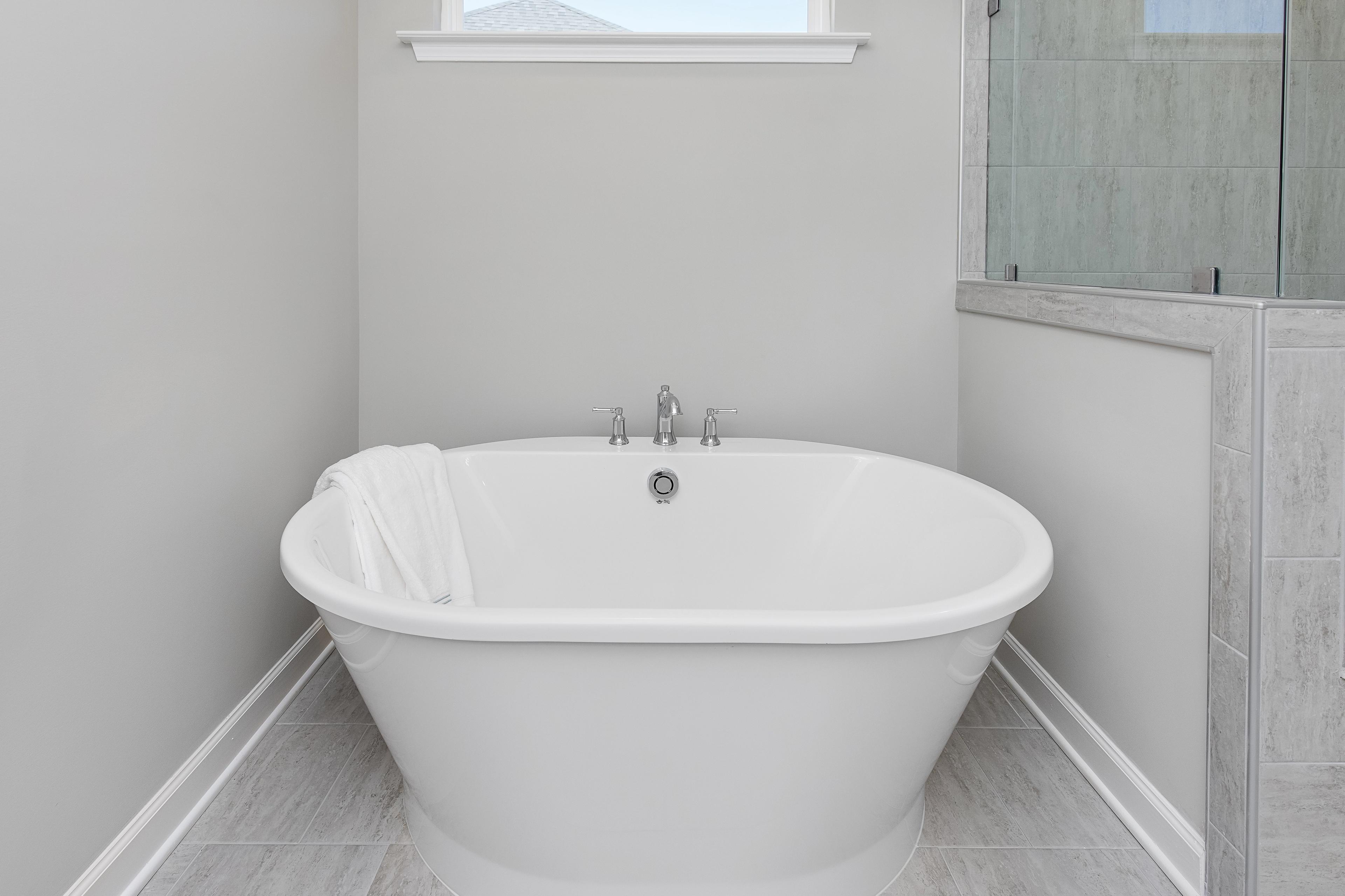 Elegant freestanding oval soaking tub with white towel in modern bathroom at Woodland Crossing, Zebulon NC by Davidson Homes