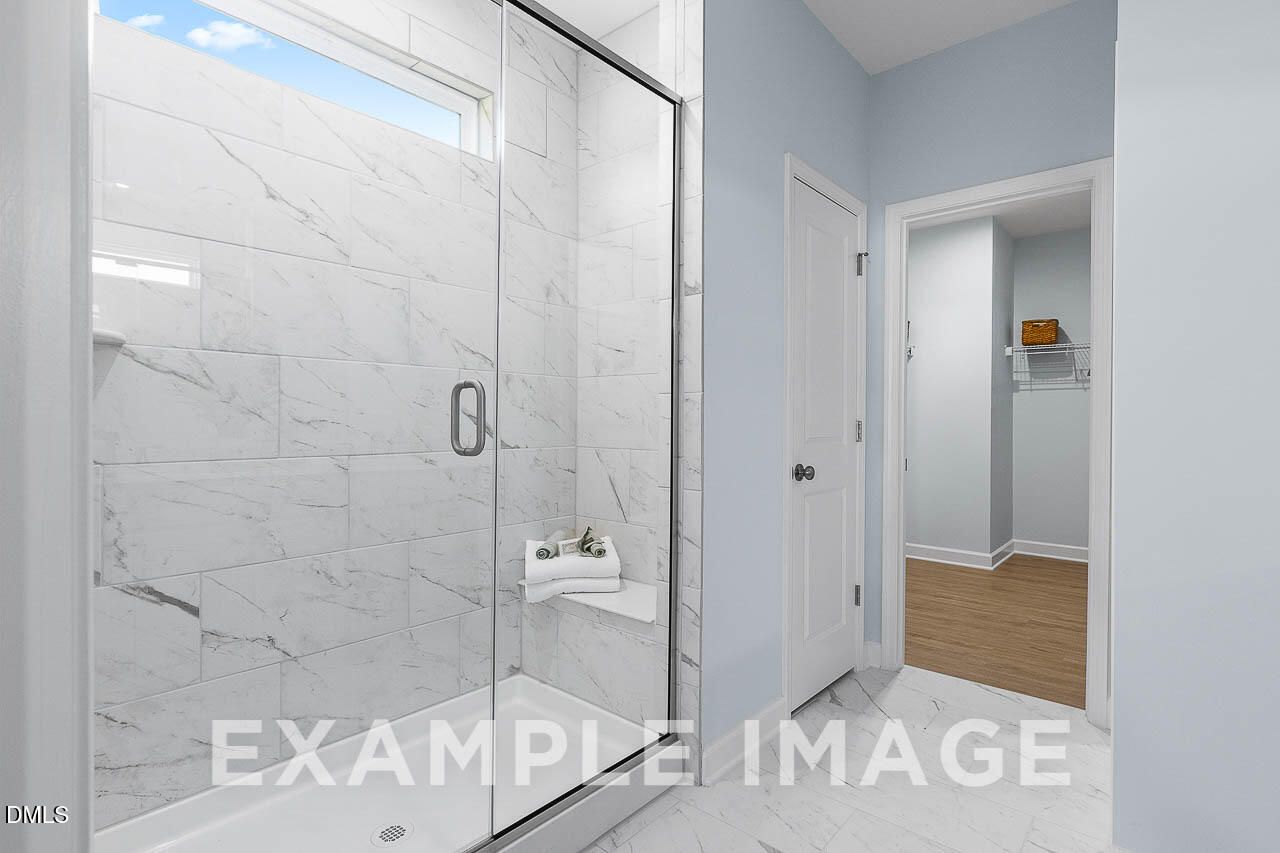 Marble-tiled walk-in shower with glass door and bench in owner's bathroom of Davidson Homes The Ash C in Lillington, NC
