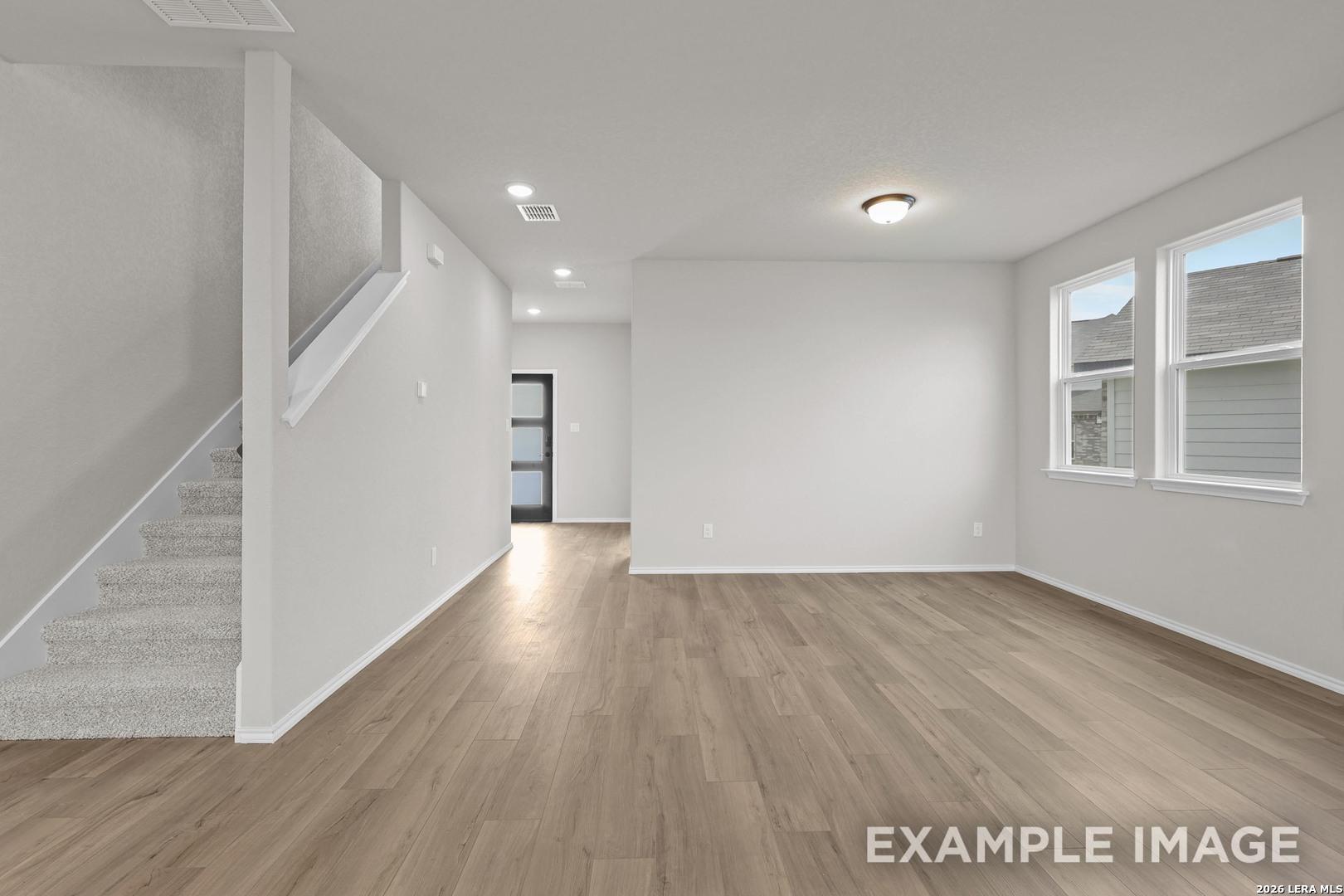 Bright open-concept living area with wood-look flooring and carpeted staircase in Davidson Homes' The Murray H, Converse, Texas