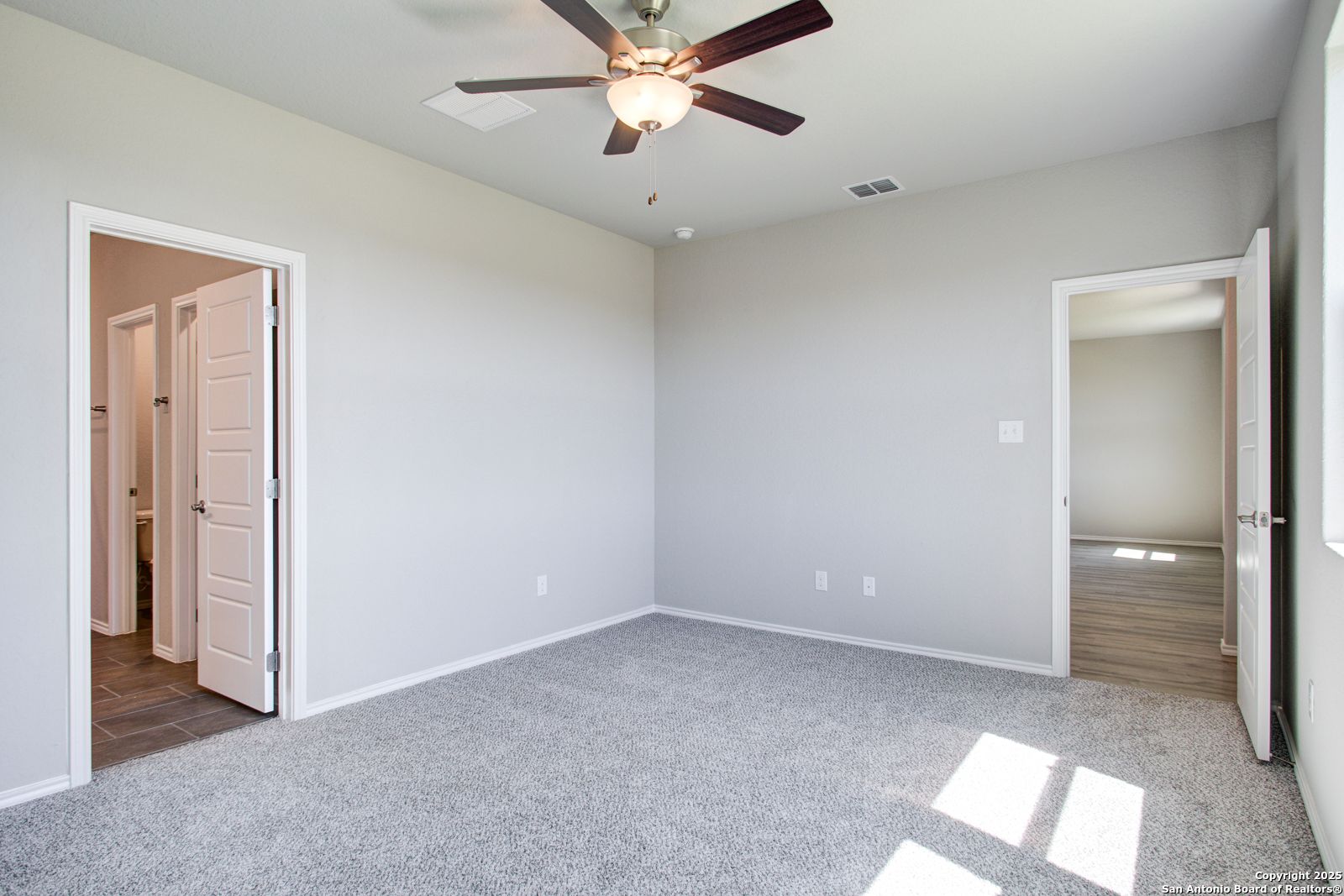 Spacious secondary bedroom with ceiling fan, gray carpet, and bath access in Davidson Homes The Douglas G, San Antonio TX