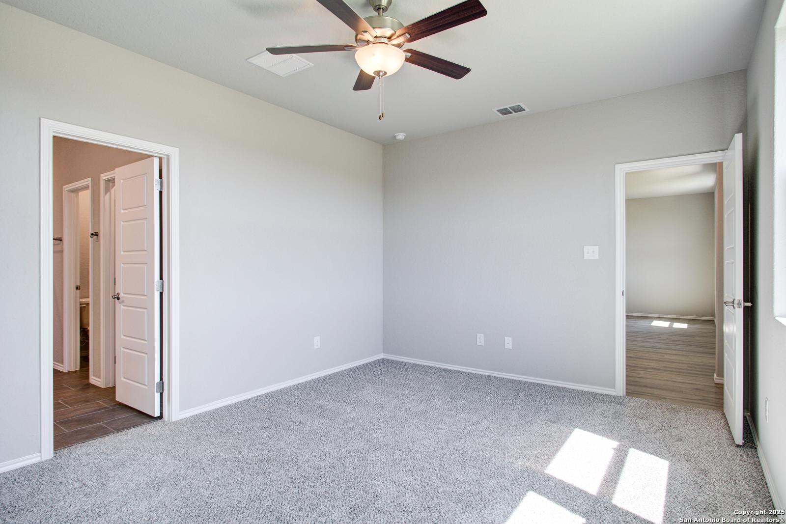 Spacious secondary bedroom with ceiling fan, gray carpet, and bath access in Davidson Homes The Douglas G, San Antonio TX