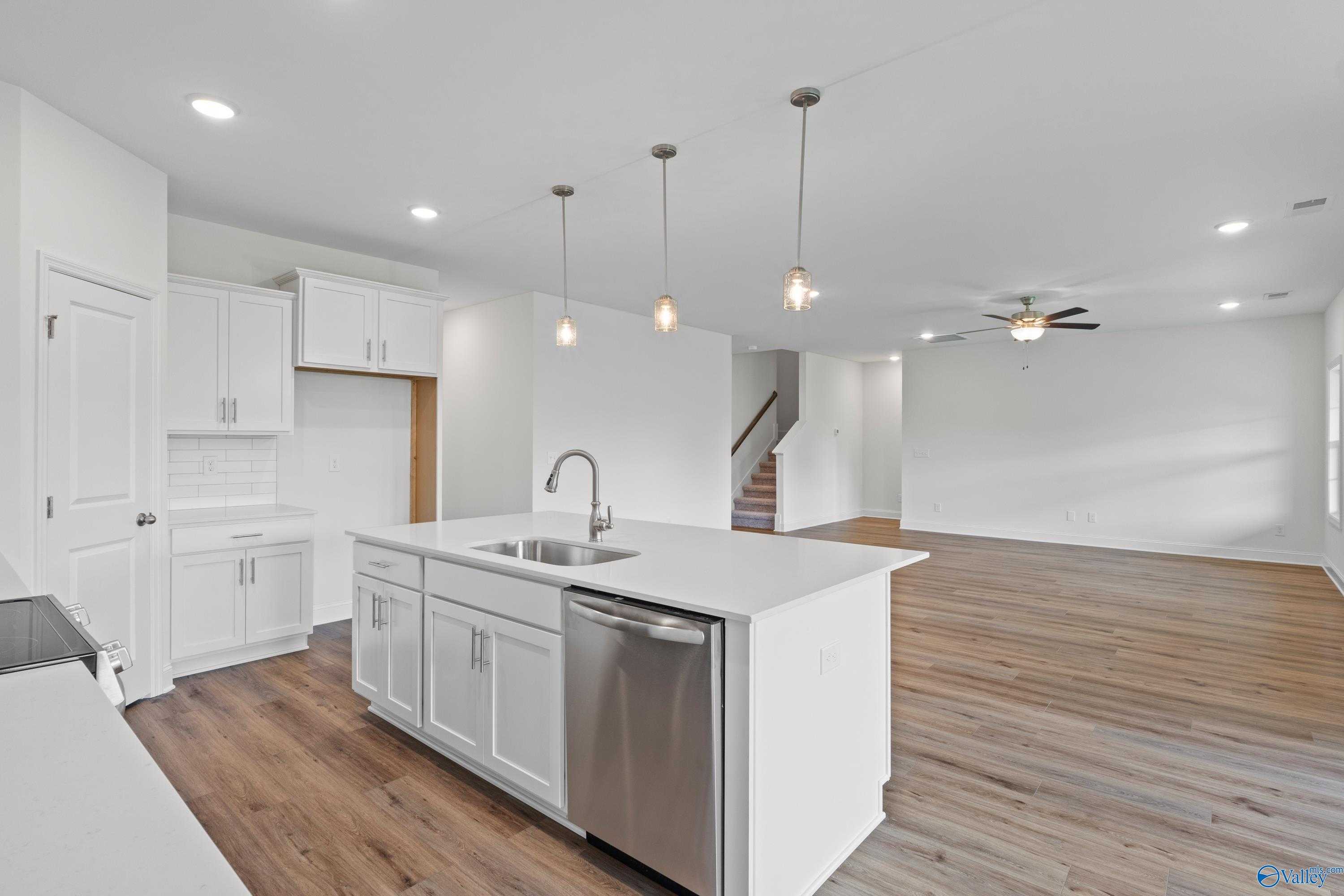Modern open-concept kitchen with white shaker cabinets, quartz island sink, stainless appliances in Davidson Homes The Rockford B, Toney, AL