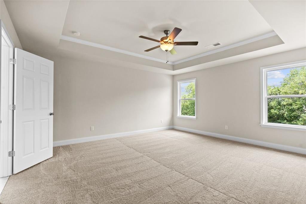 Bright bedroom with beige carpet, tray ceiling fan, and tree-view windows in Davidson Homes The Hickory B at Wehunt Meadows, Hoschton
