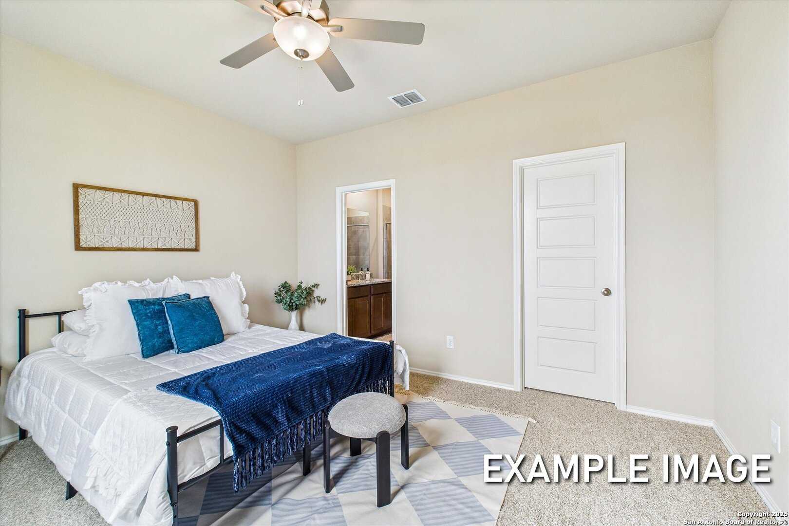 Cozy bedroom with queen bed, teal pillows, ceiling fan, and en-suite bathroom in Davidson Homes The Comal B, Agave San Antonio