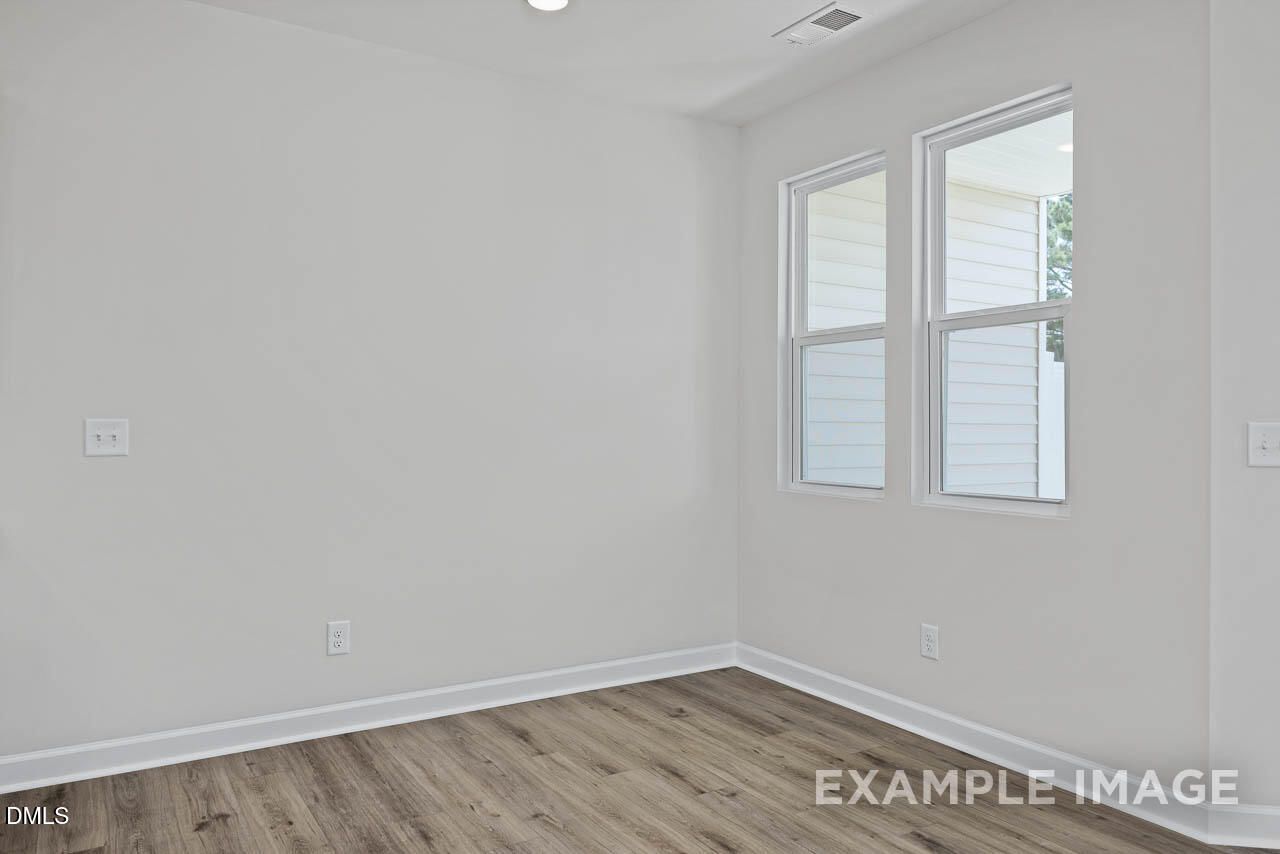 Bright, neutral bedroom with wood-style flooring in The Graham floor plan by Davidson Homes in Springvale, Fuquay-Varina.