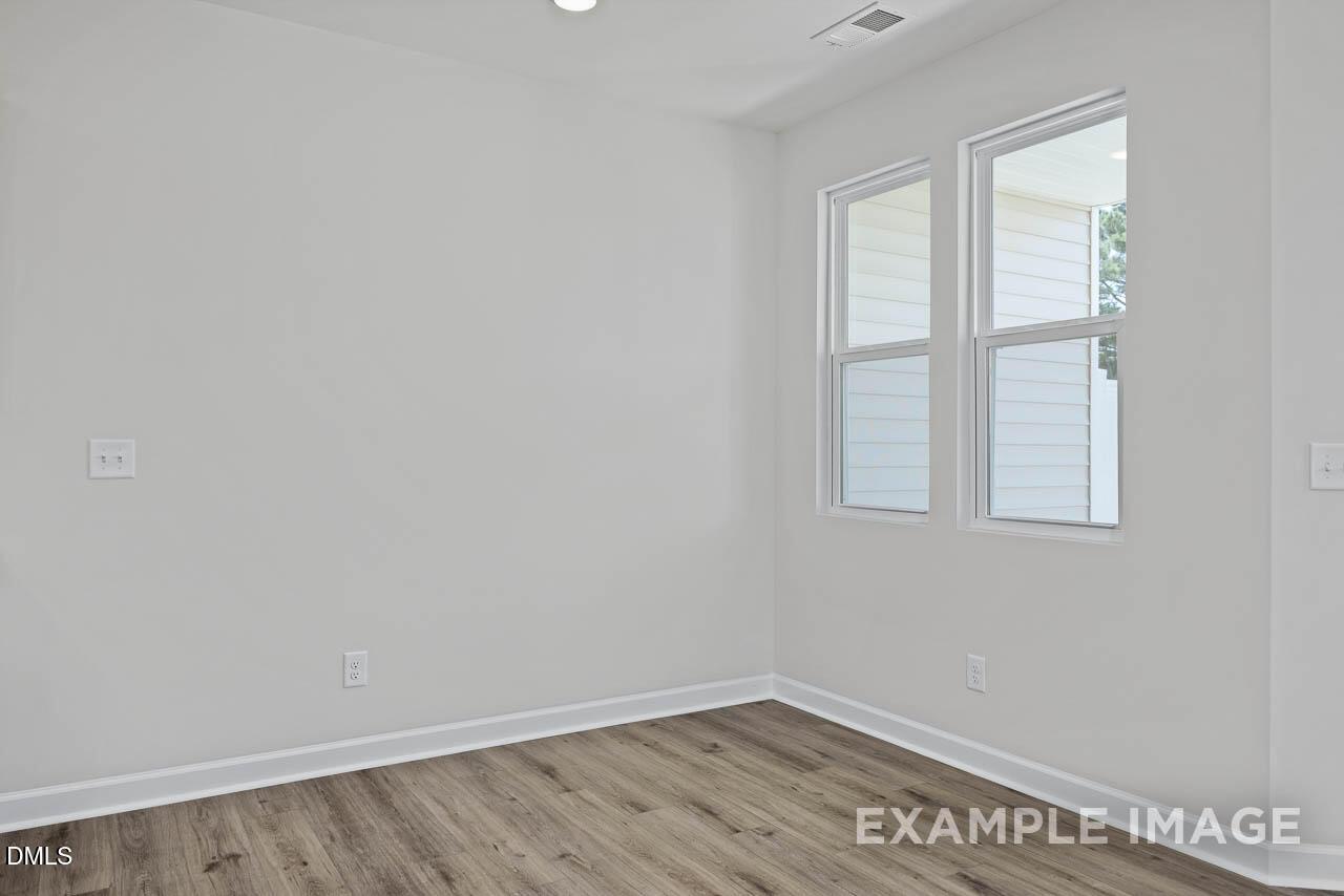 Bright, neutral bedroom with wood-style flooring in The Graham floor plan by Davidson Homes in Springvale, Fuquay-Varina.