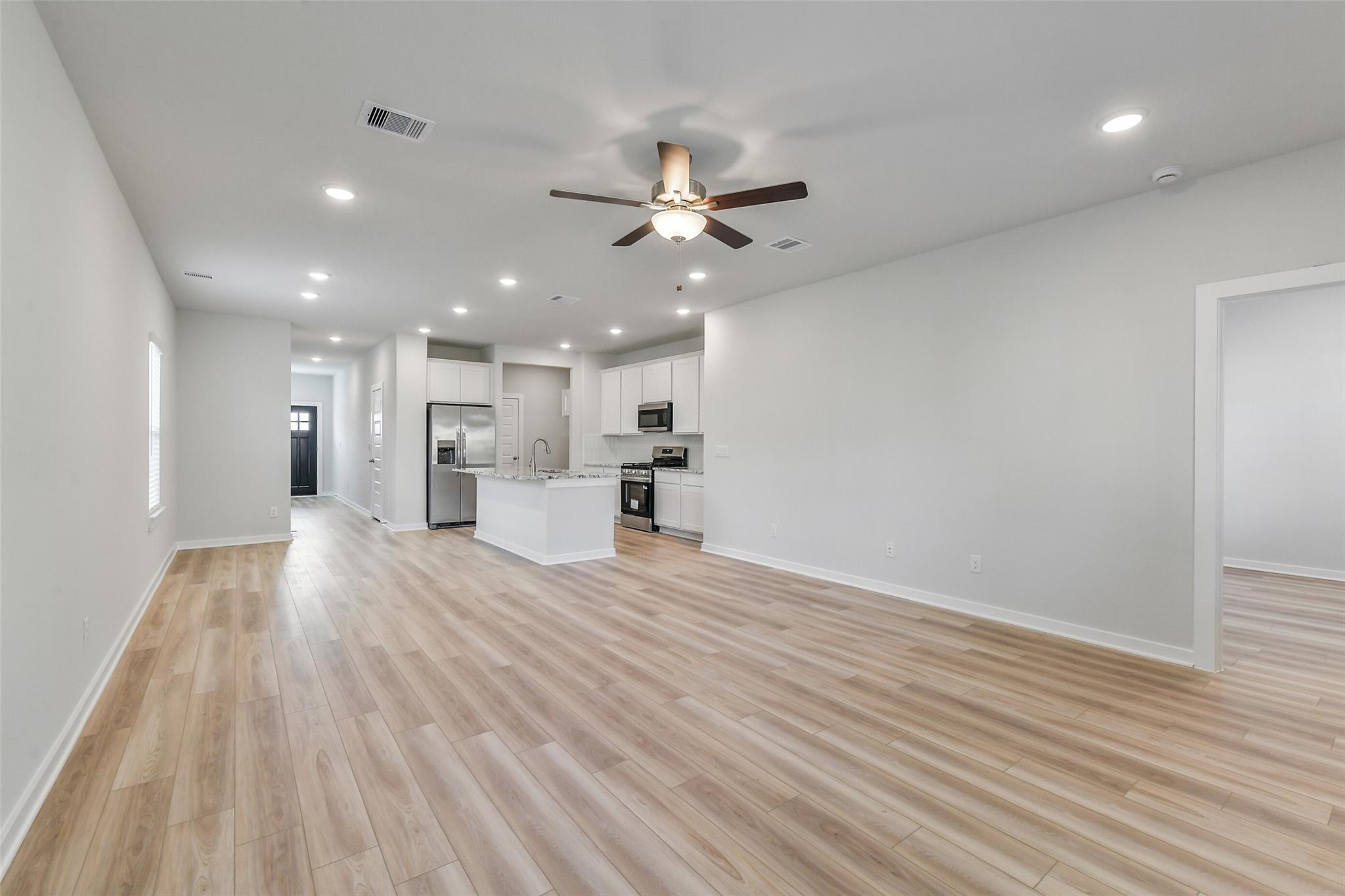 Open-concept living room and kitchen with hardwood floors, white cabinets, and stainless appliances in Davidson Homes The Brazos F, Magnolia, Texas
