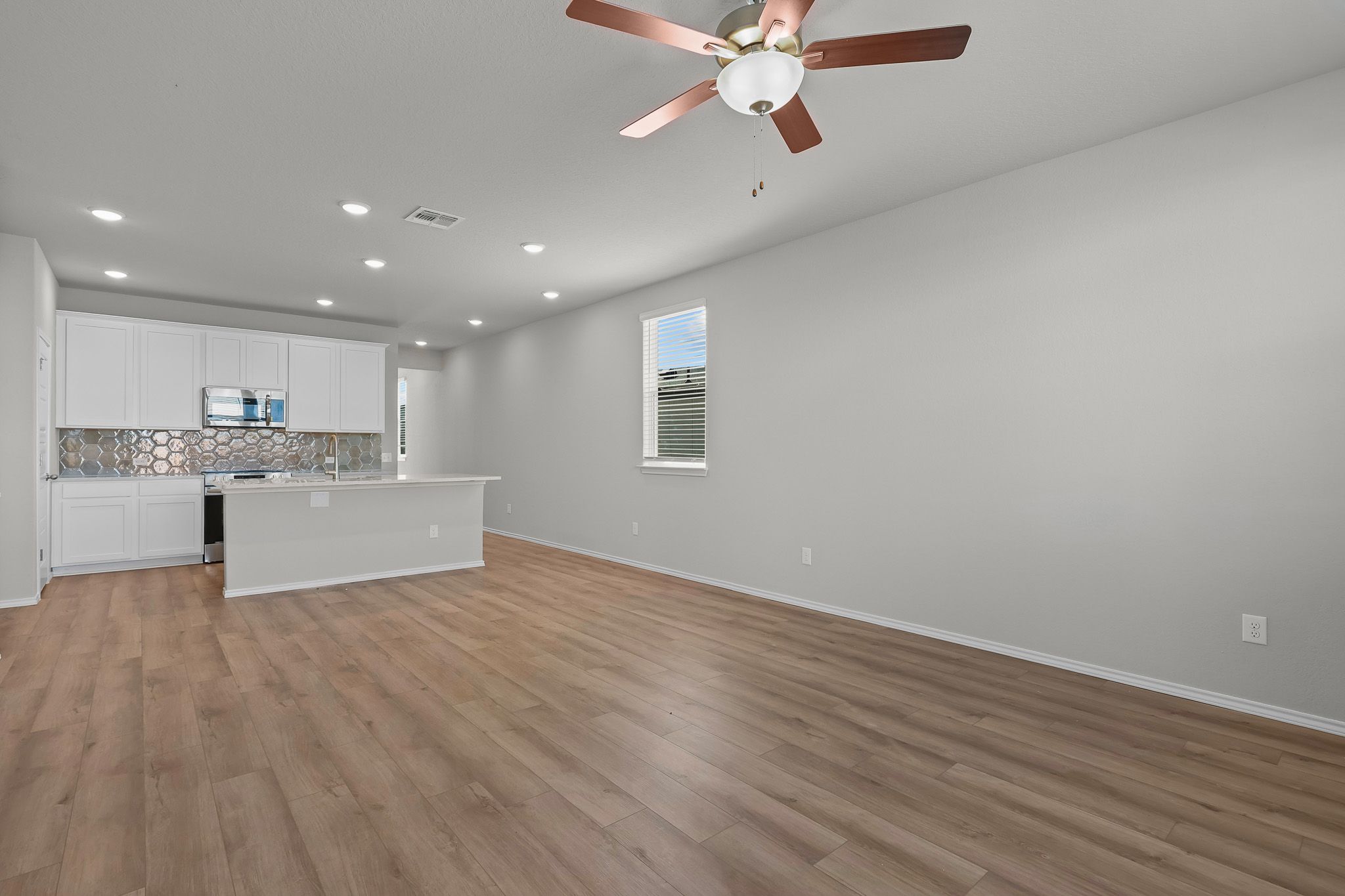 Open-concept kitchen and living area in The Colorado B featuring white cabinetry, wood-look flooring, and ceiling fan.