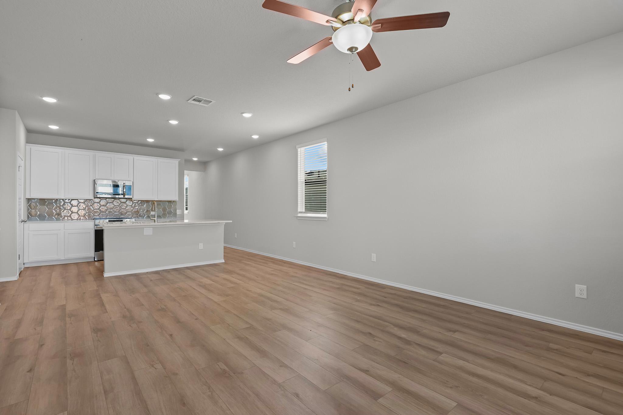 Open-concept kitchen and living area in The Colorado B featuring white cabinetry, wood-look flooring, and ceiling fan.
