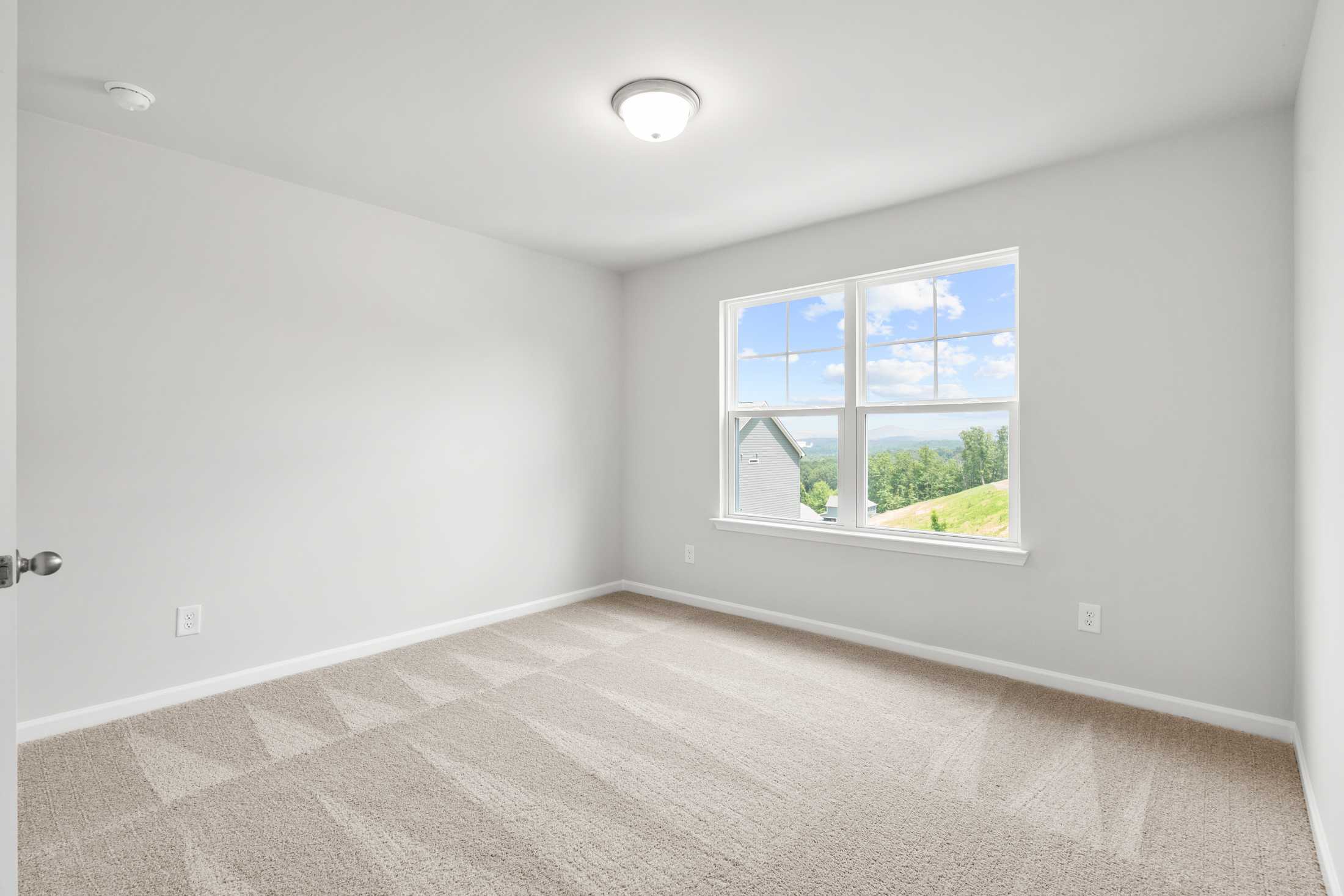 Spacious secondary bedroom in The Ash B at Wehunt Meadows featuring light gray walls, beige carpet, and large window with green hill view