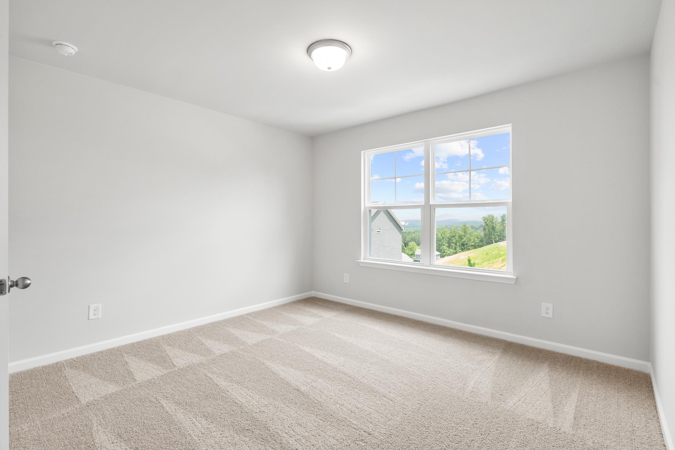 Spacious secondary bedroom in The Ash B at Wehunt Meadows featuring light gray walls, beige carpet, and large window with green hill view