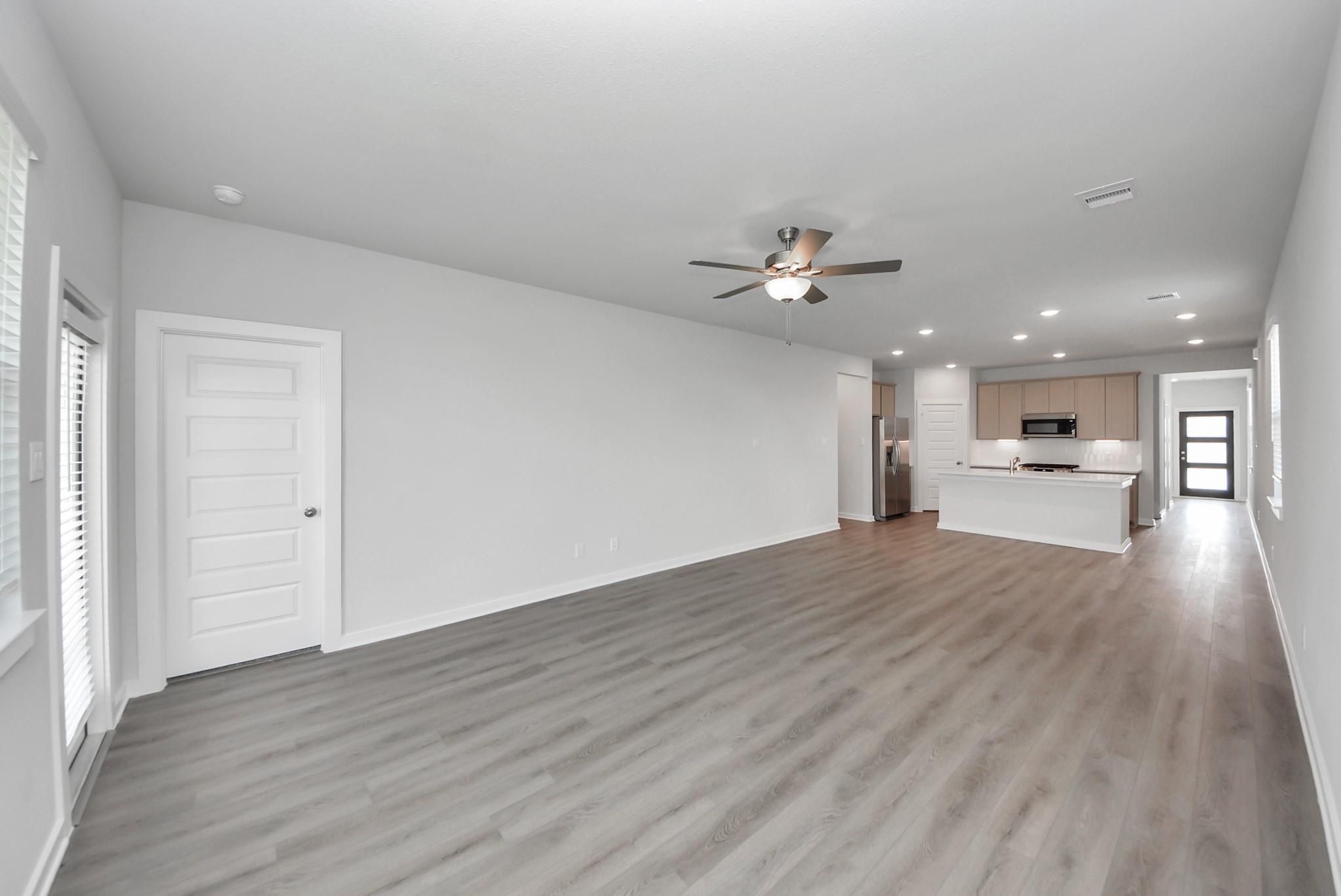 Open-concept living area with luxury vinyl plank flooring, ceiling fan, and kitchen island in Davidson Homes The San Marcos E, Beasley, TX