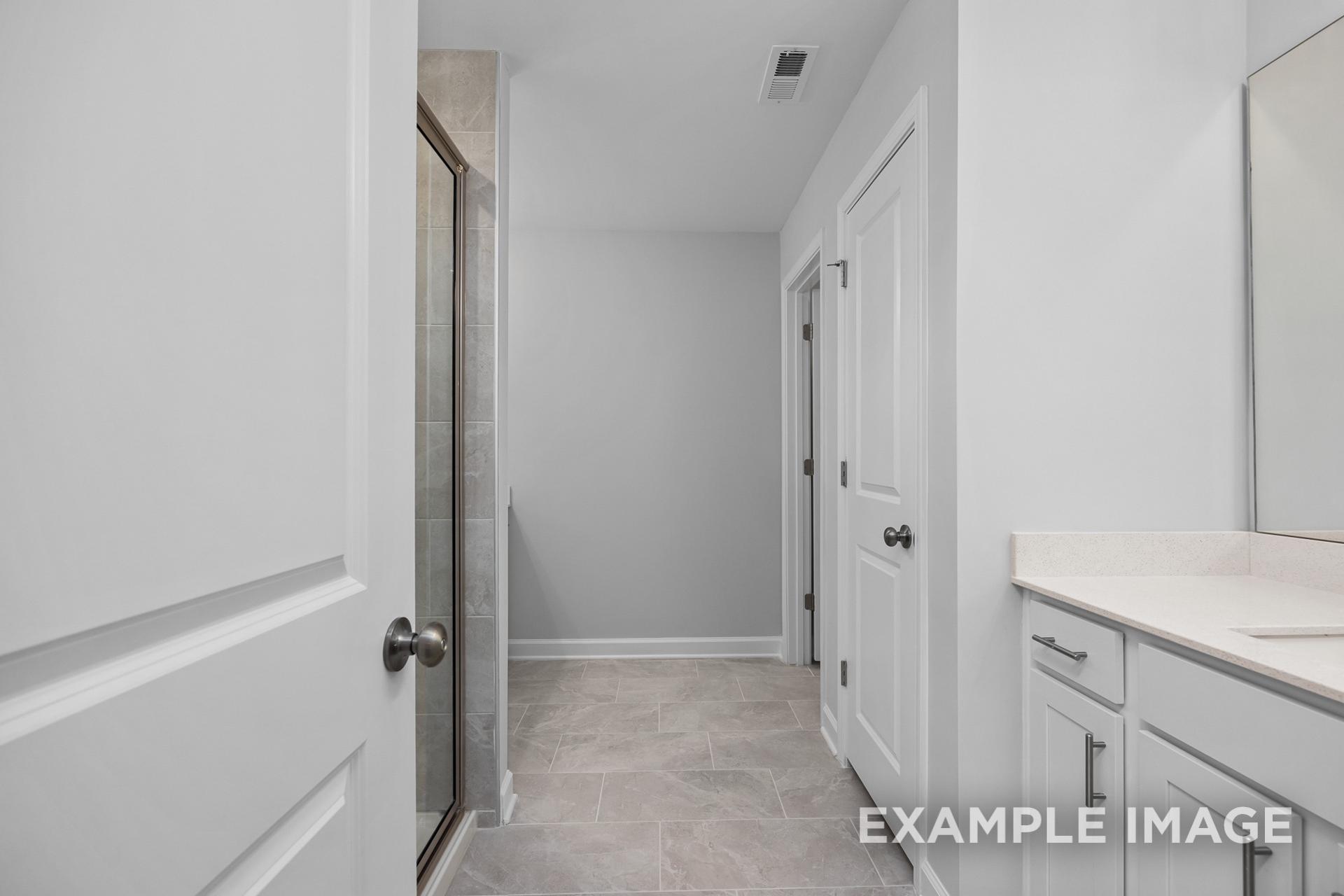 Spacious master bathroom in The Preston B featuring walk-in glass shower, double vanity, and neutral tile flooring