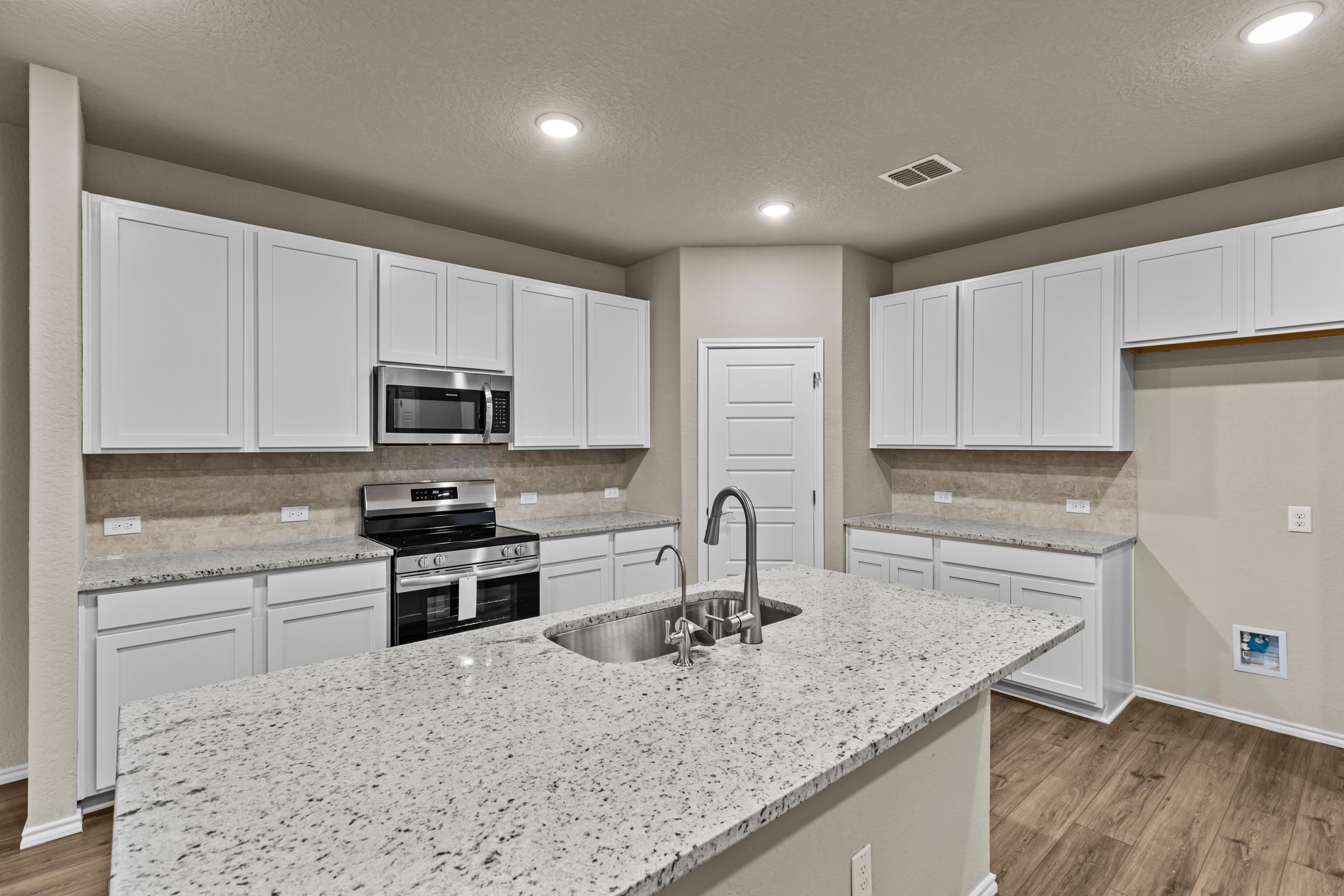 Modern white kitchen with granite island, stainless appliances, and subway tile backsplash in Davidson Homes The Douglas F, San Antonio