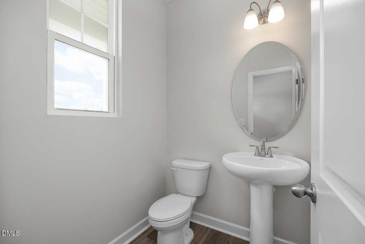 Elegant powder room featuring pedestal sink, round mirror, white toilet in Davidson Homes The Warren, Fuquay-Varina, NC
