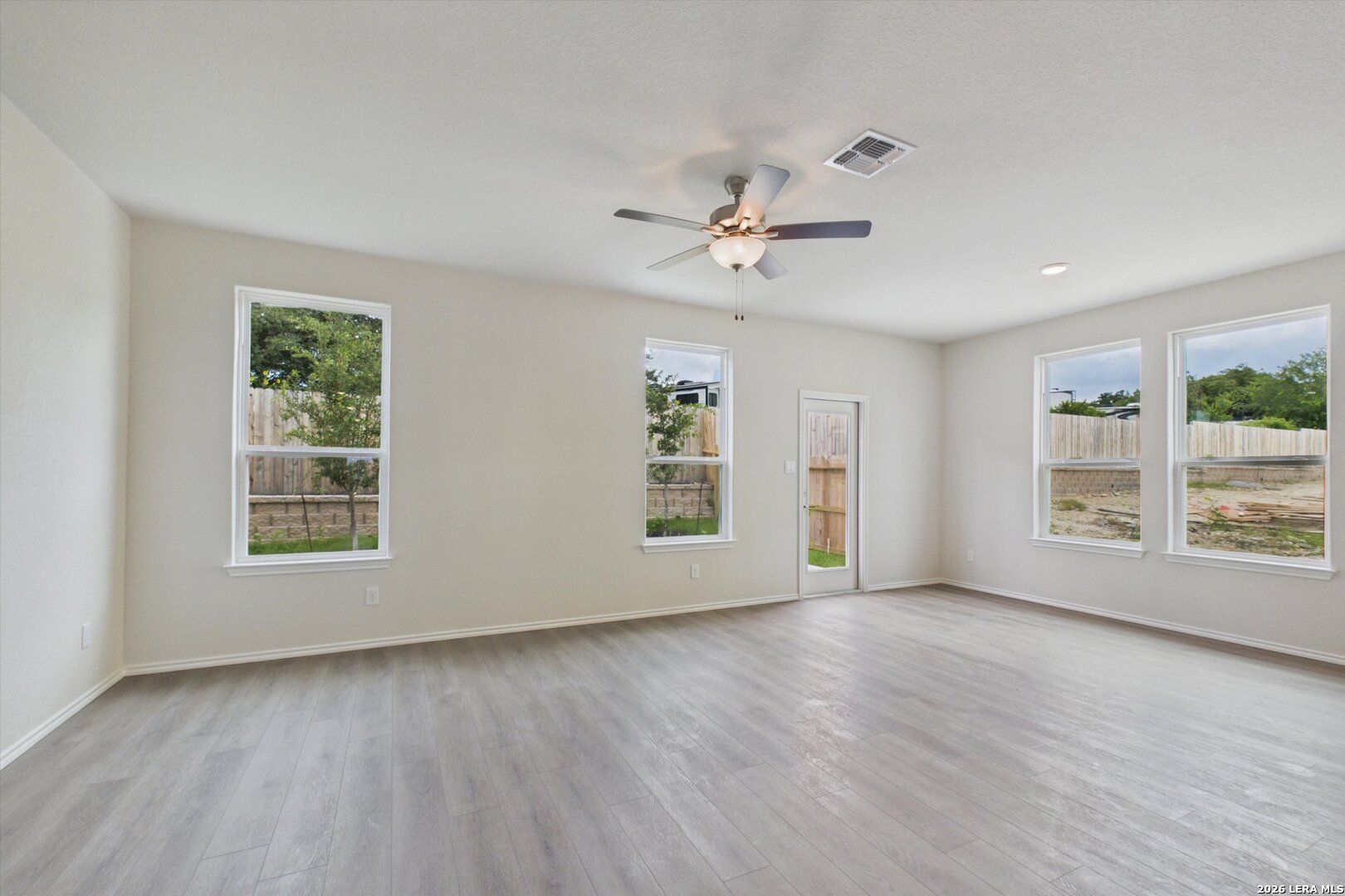 Spacious, sunlit living area with luxury vinyl plank flooring and ceiling fan in The Charlotte B at Meadows at Oak Creek.