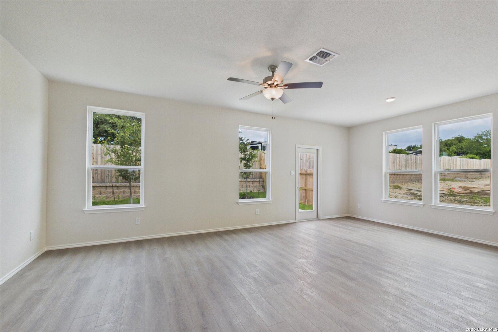 Spacious, sunlit living area with luxury vinyl plank flooring and ceiling fan in The Charlotte B at Meadows at Oak Creek.