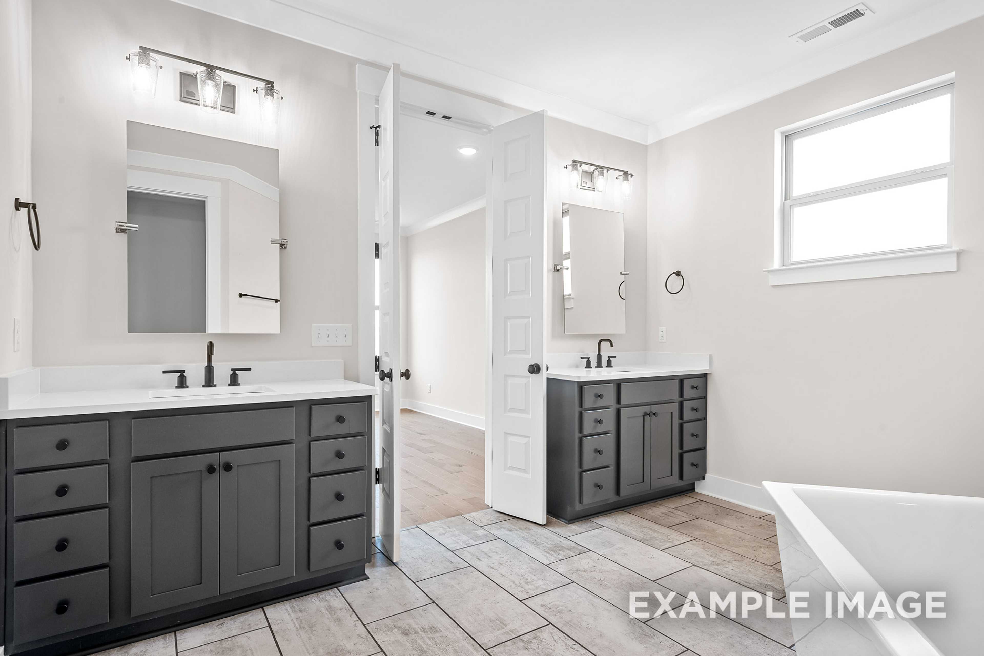 Spacious master bathroom in The Hawkins with dual gray vanities, freestanding tub, and open bedroom access