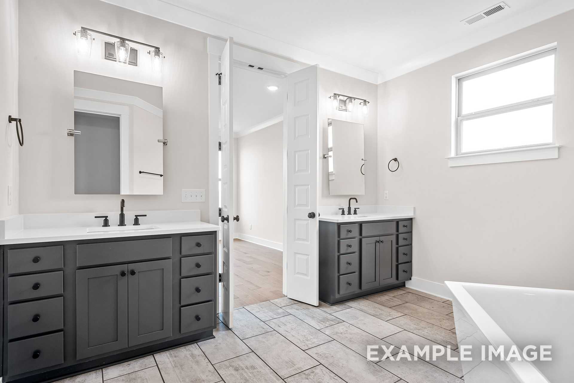 Spacious master bathroom in The Hawkins with dual gray vanities, freestanding tub, and open bedroom access