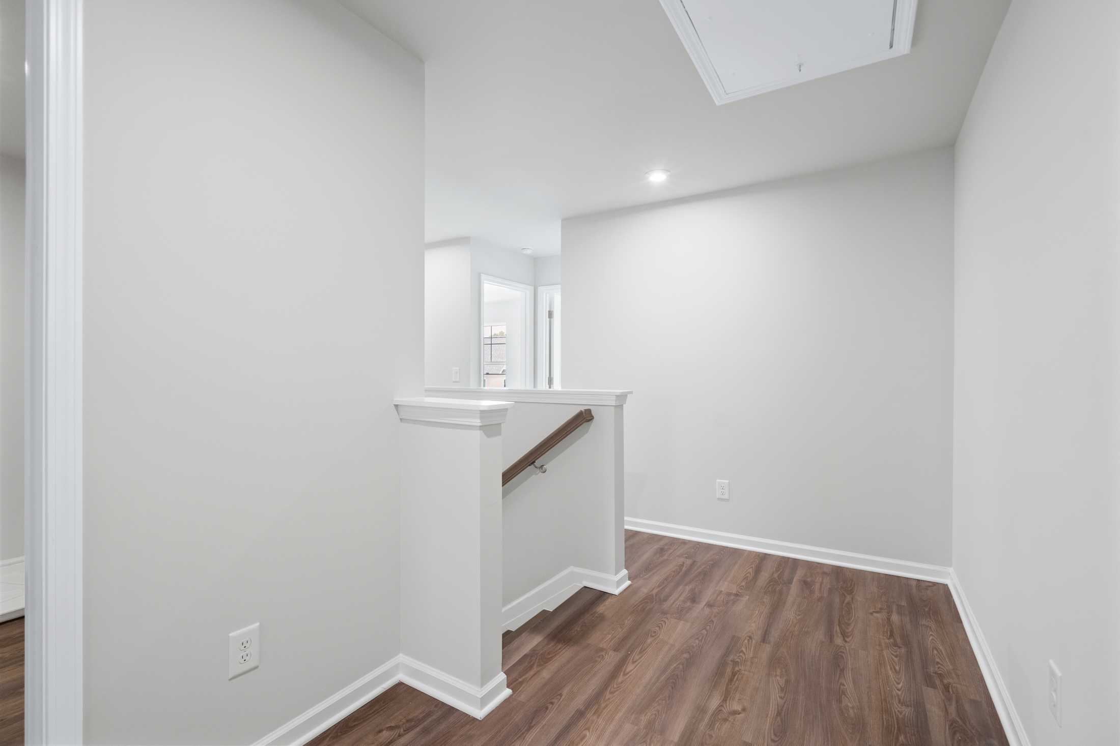 Spacious upper hallway in The Cary A 2-story home with white walls, light oak floors, skylight, and overlook railing