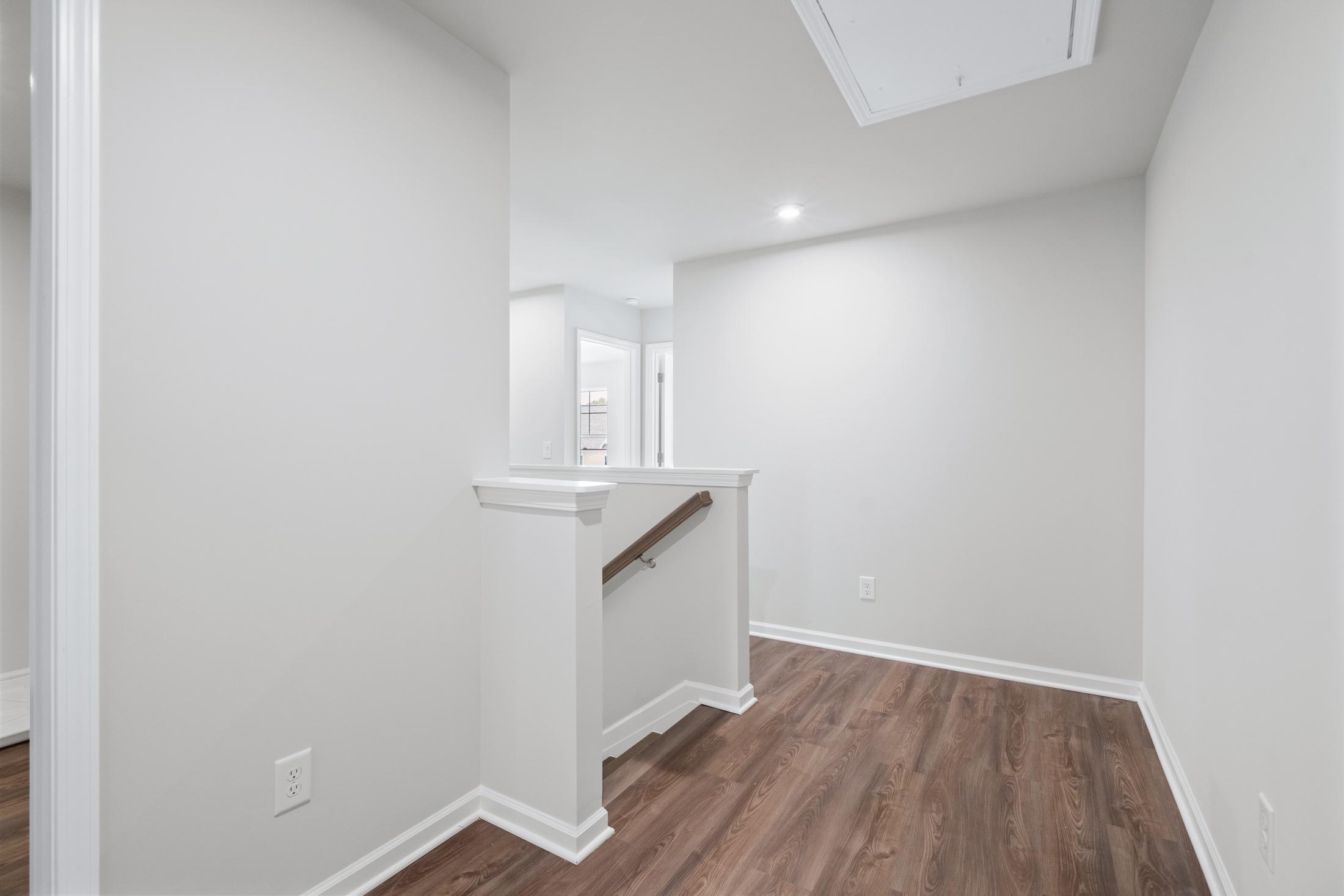 Spacious upper hallway in The Cary A 2-story home with white walls, light oak floors, skylight, and overlook railing