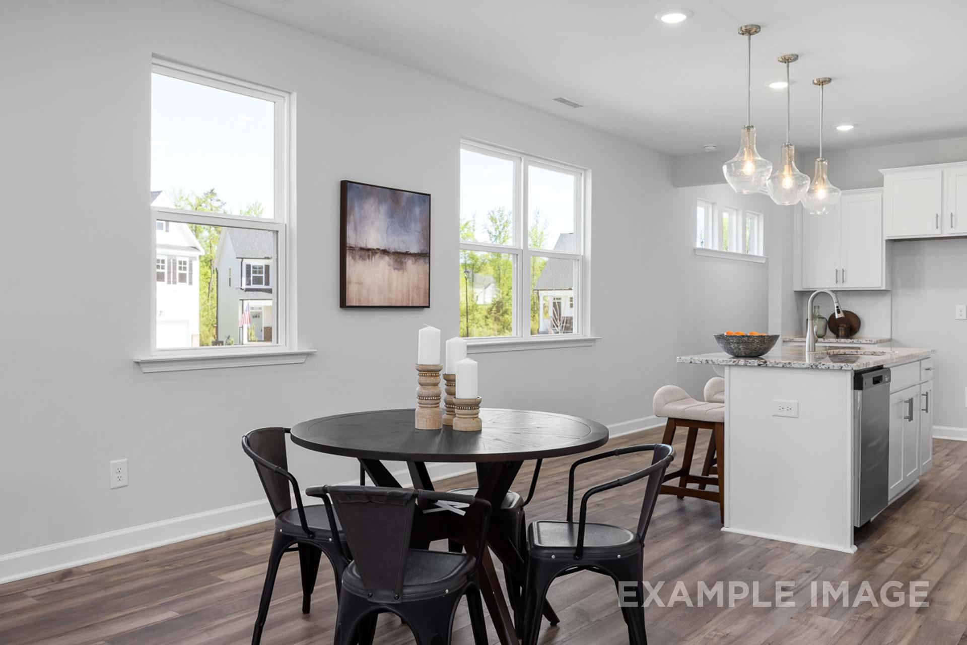 Open-concept dining area in The Carter B showcasing round wooden table with black chairs, adjacent white kitchen cabinets, pendant lights