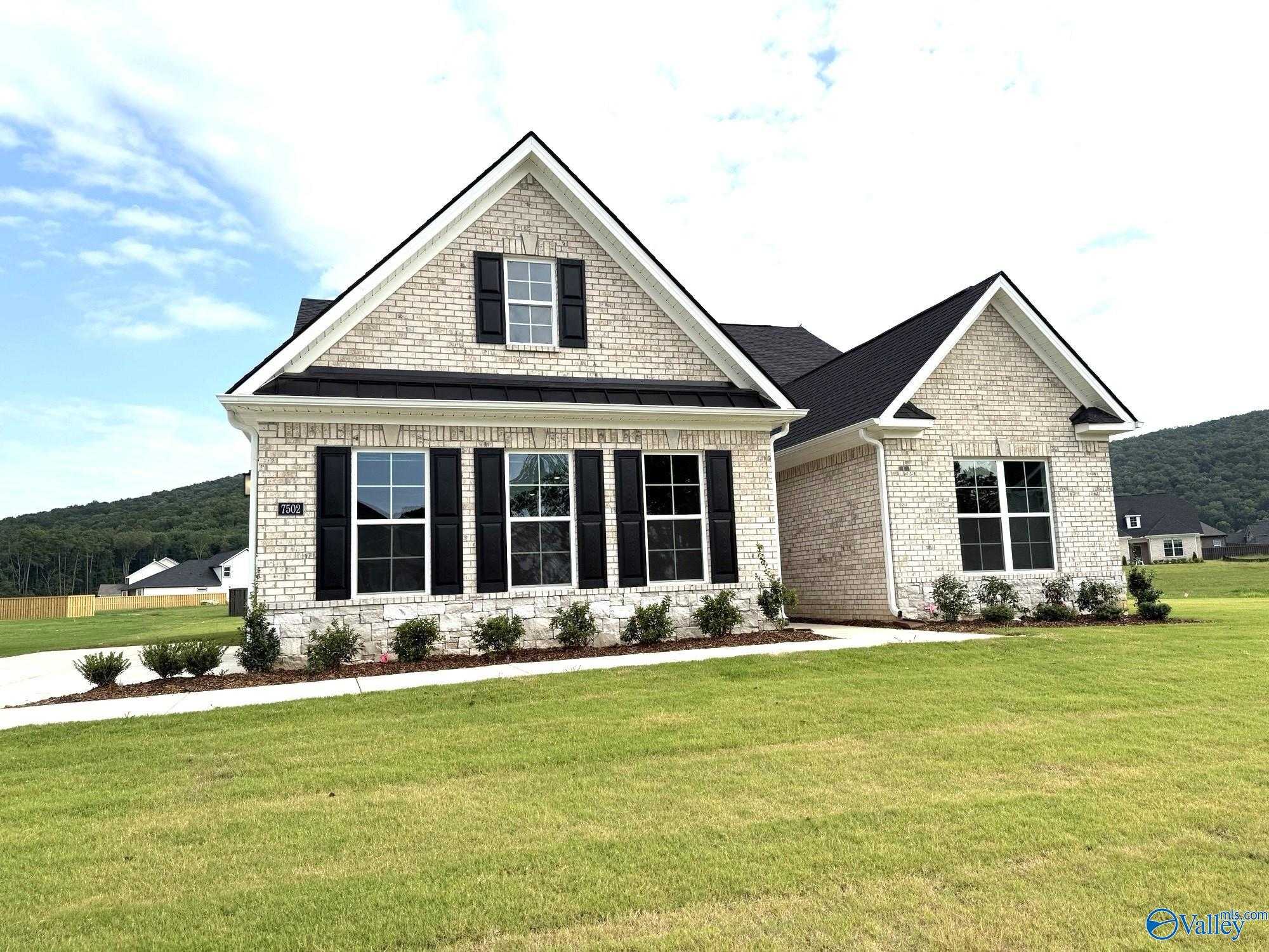 Evermore Homes The Oxford: White brick 1.5-story exterior with black shutters, gabled roof, and lush landscaping in The Meadows at Hampton Cove, Owens Cross Roads, Alabama