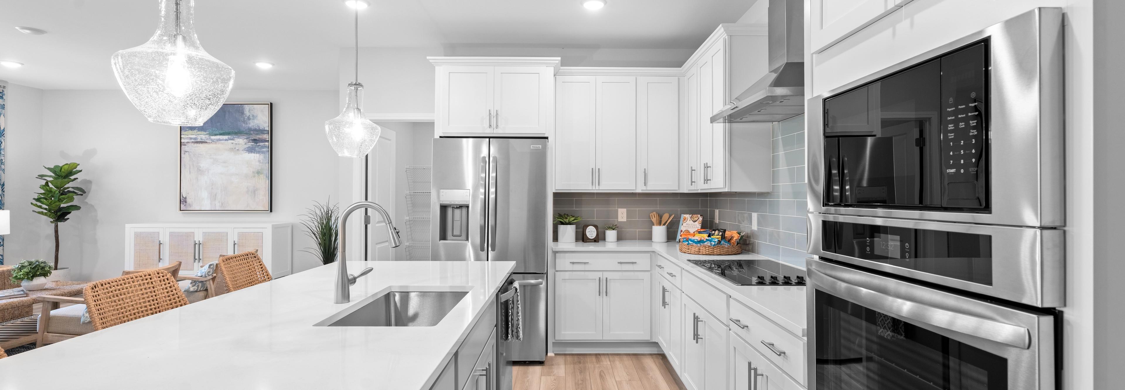 Spacious open-concept kitchen and living room in Links Crossing Auburn Alabama with white cabinets, plush beige sofa, orange ottoman, and fiddle leaf fig plant