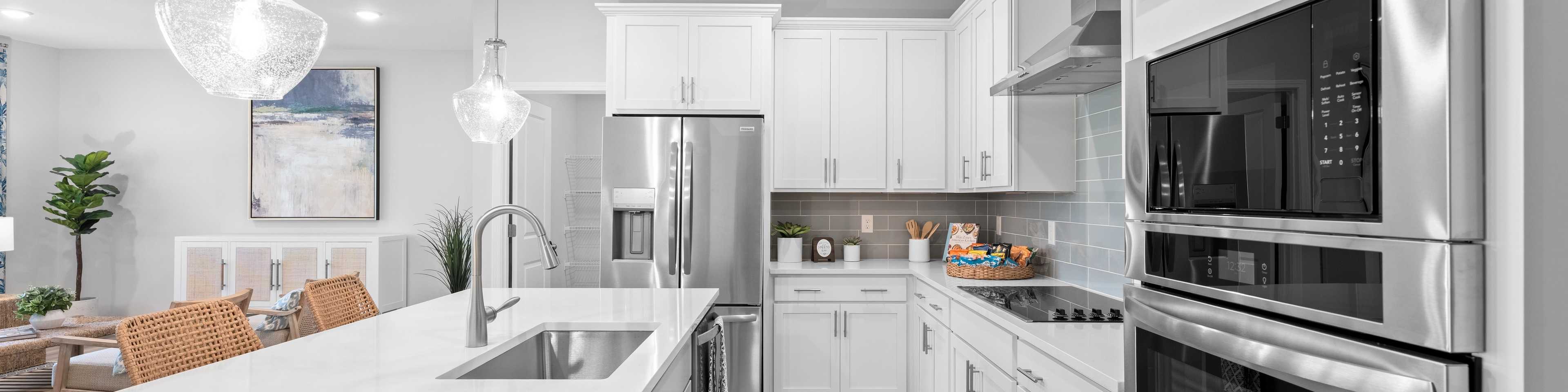 Spacious open-concept kitchen and living room in Links Crossing Auburn Alabama with white cabinets, plush beige sofa, orange ottoman, and fiddle leaf fig plant