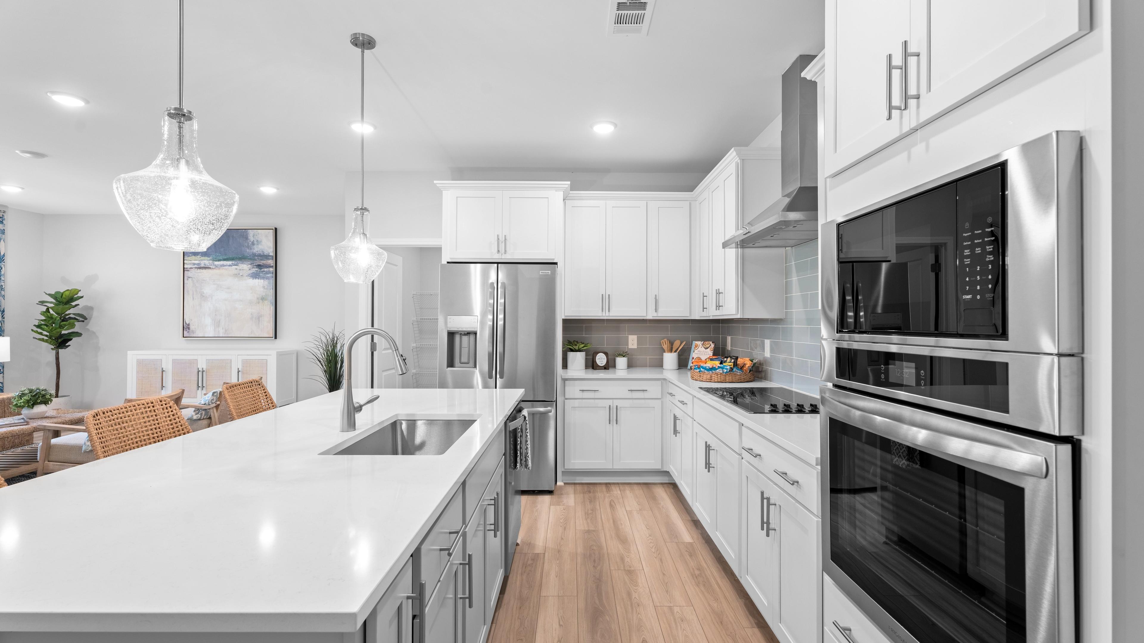 Spacious open-concept kitchen and living room in Links Crossing Auburn Alabama with white cabinets, plush beige sofa, orange ottoman, and fiddle leaf fig plant