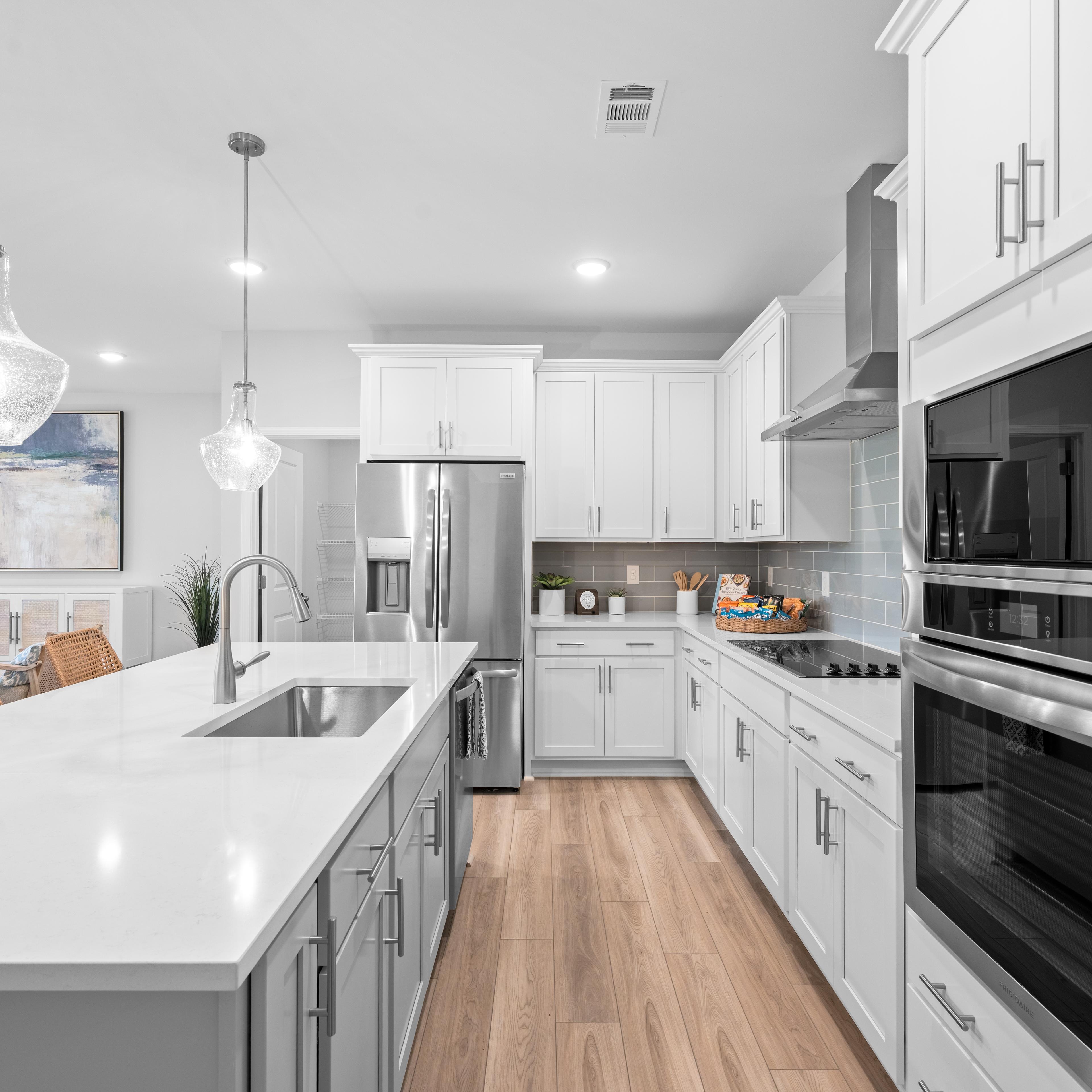 Spacious open-concept kitchen and living room in Links Crossing Auburn Alabama with white cabinets, plush beige sofa, orange ottoman, and fiddle leaf fig plant