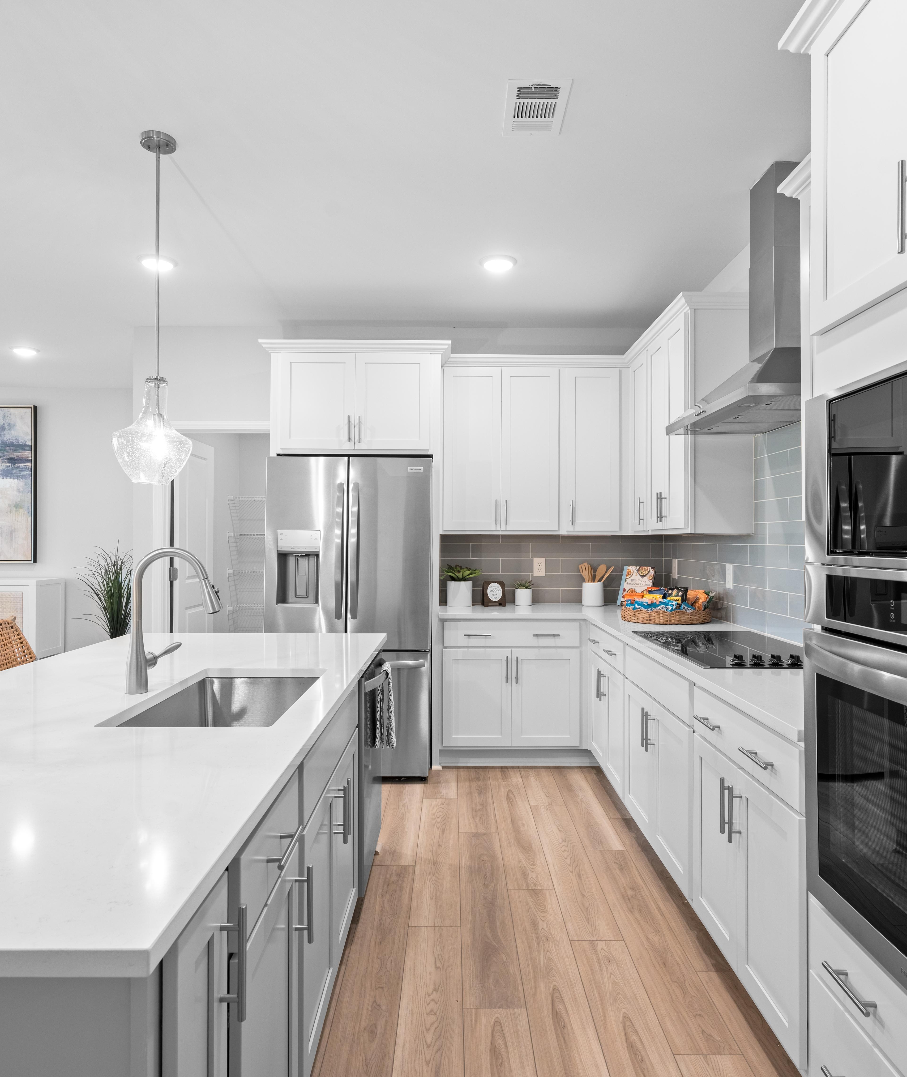 Open-concept kitchen and living room at Anderson Lakes in Opelika Alabama with hardwood floors white cabinets island bar and large windows