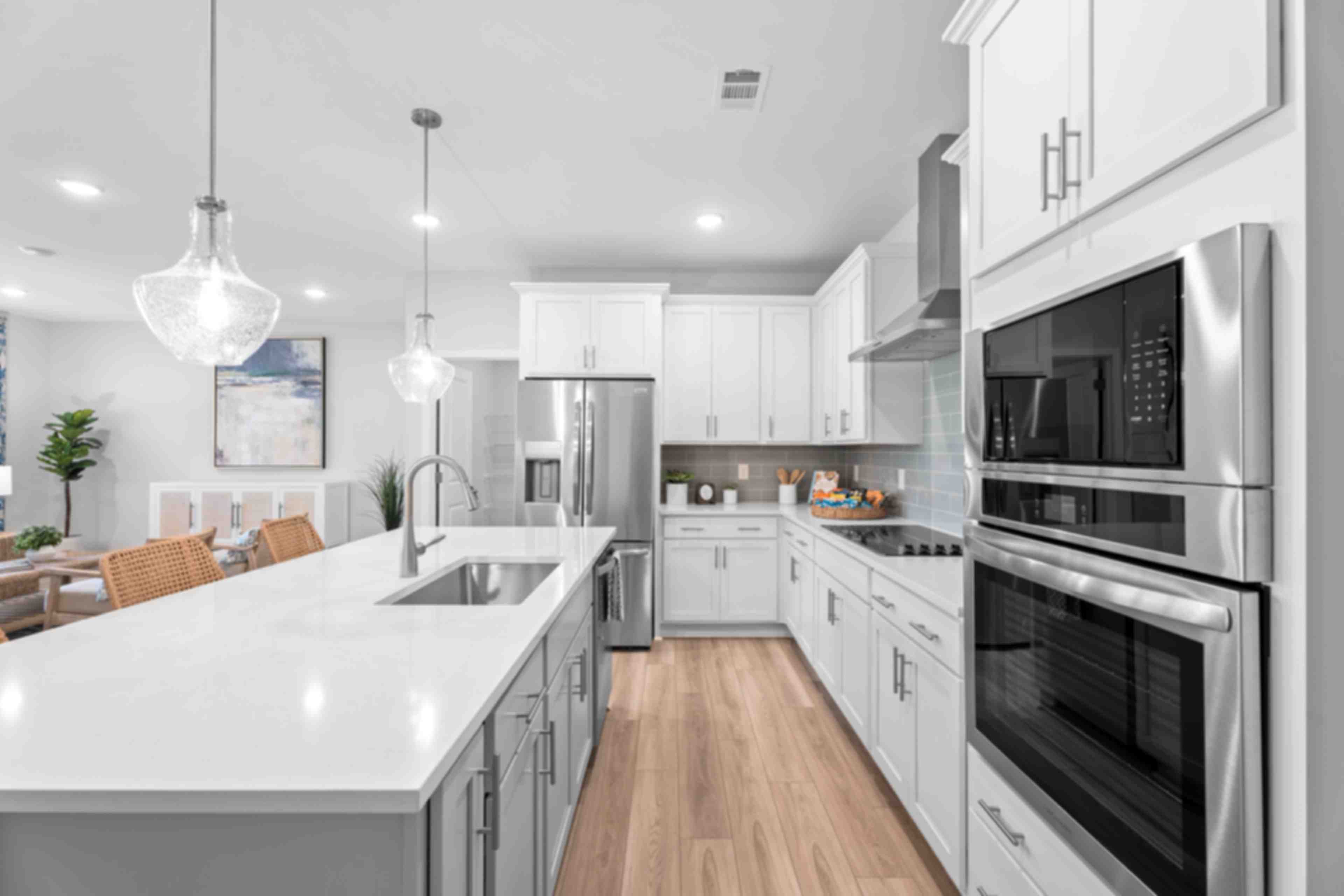 Spacious open-concept kitchen and living room in Links Crossing Auburn Alabama with white cabinets, plush beige sofa, orange ottoman, and fiddle leaf fig plant