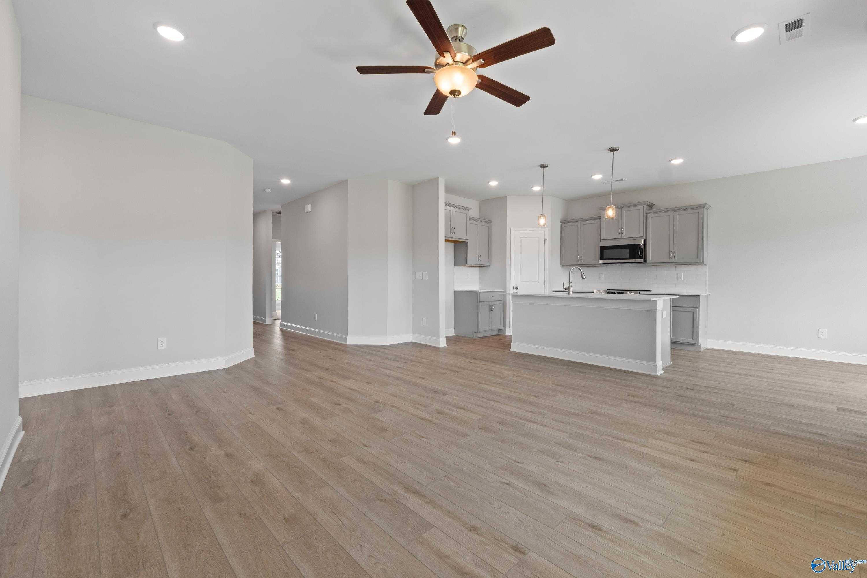 Open-concept kitchen-living area with gray cabinets, island, ceiling fan, and hardwood floors in The Asheville by Davidson Homes, Meridianville, AL