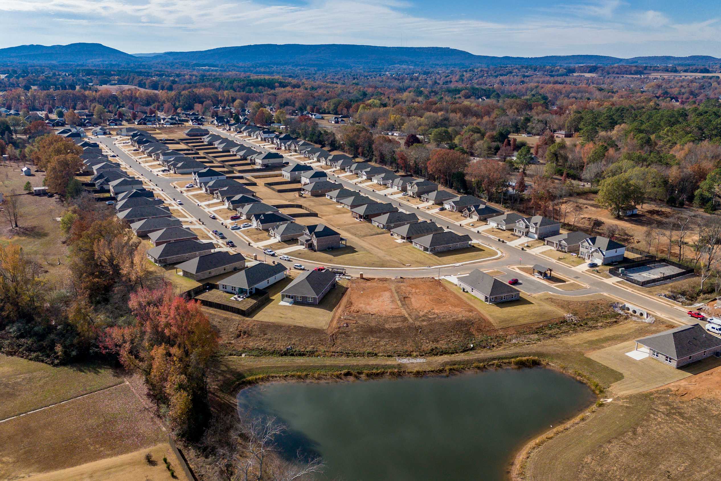 Aerial view of Flint Meadows neighborhood in New Market Alabama with new homes, autumn foliage, and serene pond