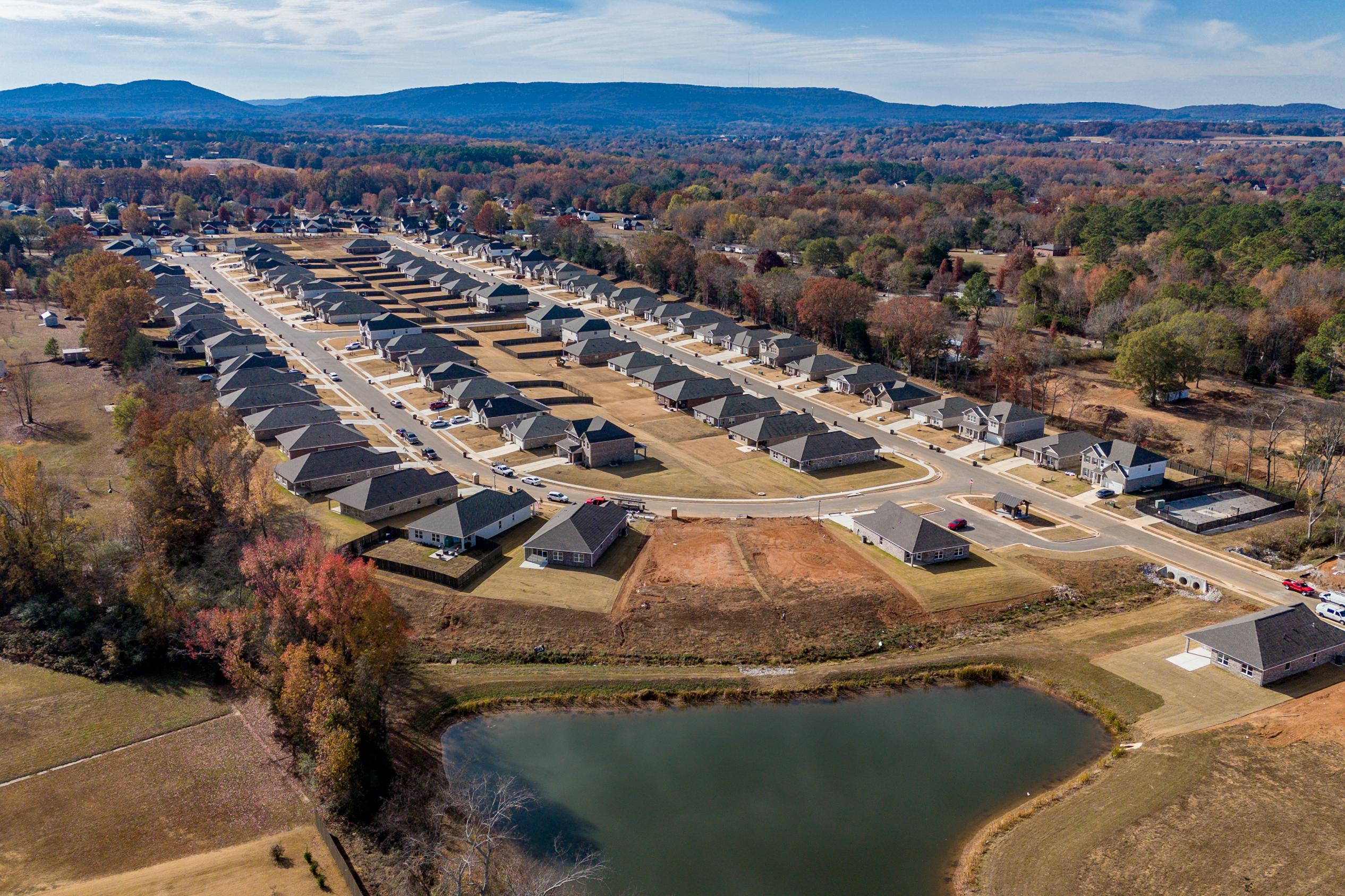 Aerial view of Flint Meadows neighborhood in New Market Alabama with new homes, autumn foliage, and serene pond